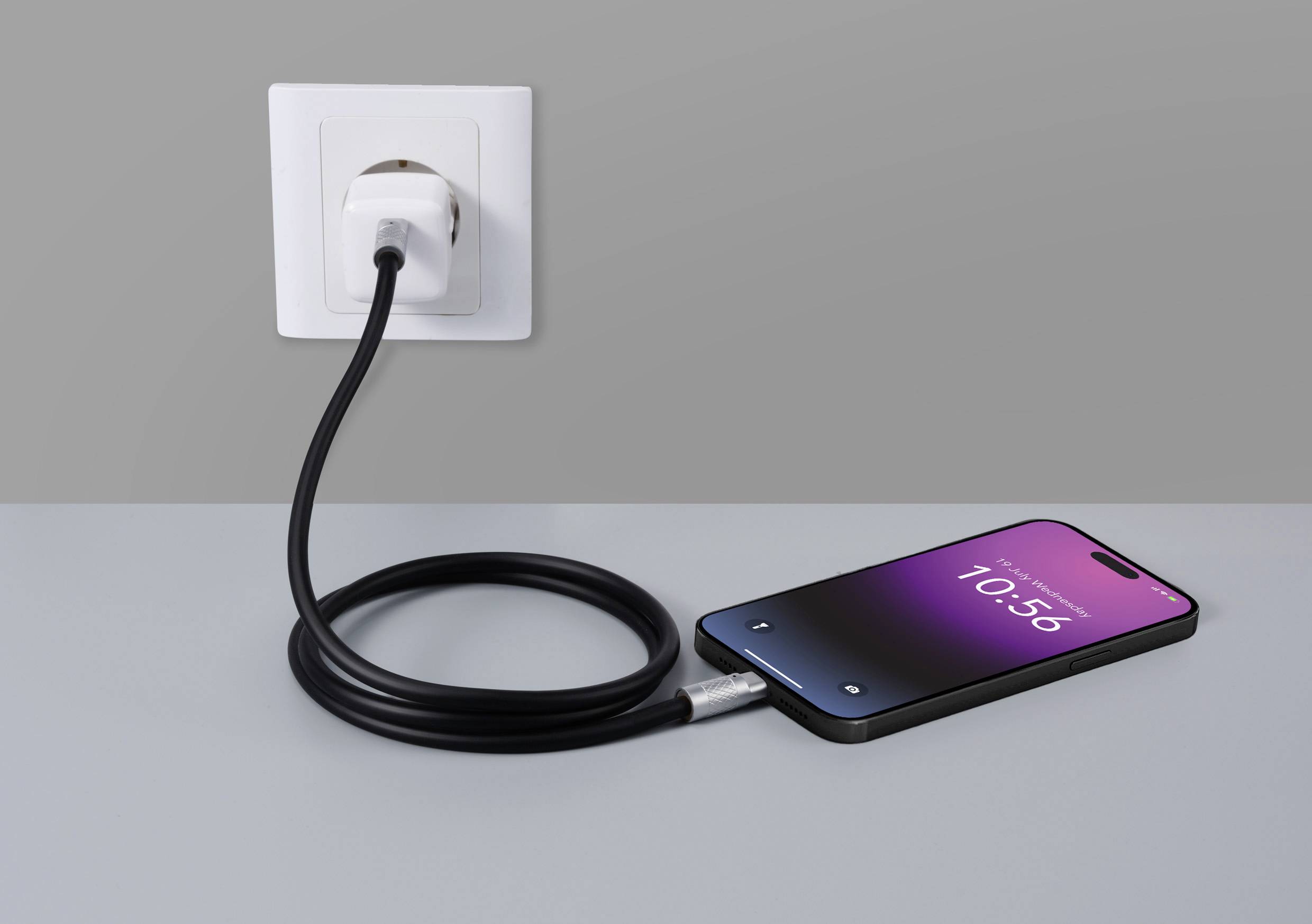 Smartfon z ekranem ładowania leży na stole i jest podłączony czarnym przewodem do gniazdka ściennego.