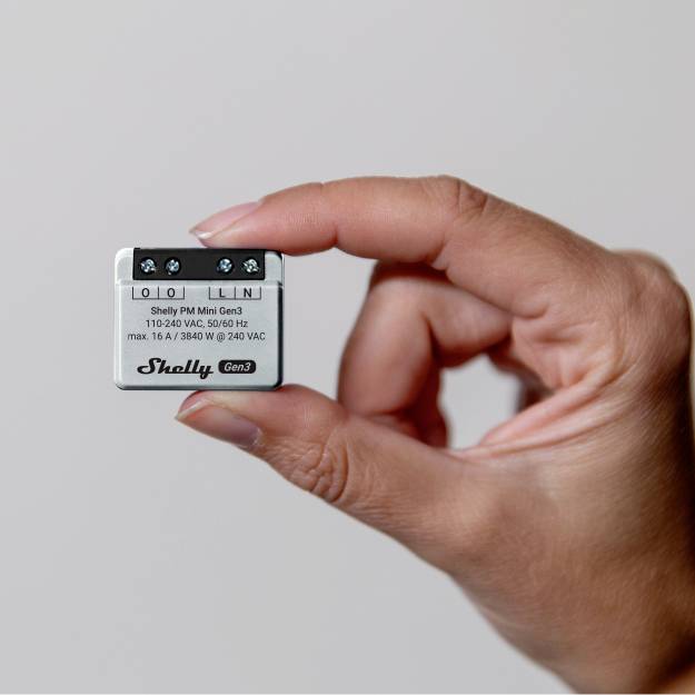 Ręka trzyma przekaźnik Shelly Plus, białe oznaczenie informacji o podłączeniu, ograniczony widok urządzenia.