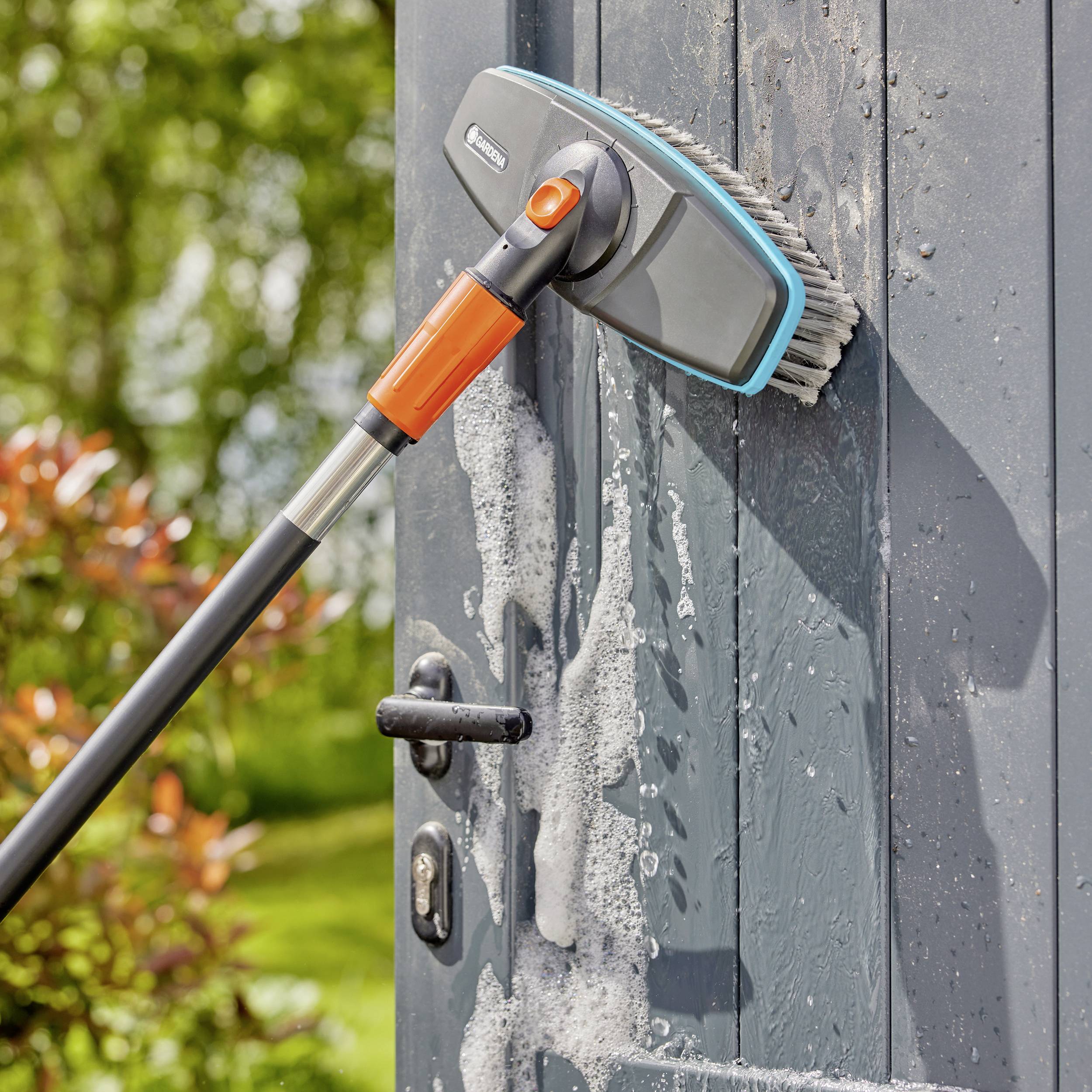 Niebieskie drzwi są szorowane długą szczotką do czyszczenia z mydłem. W tle widać zielony ogród.