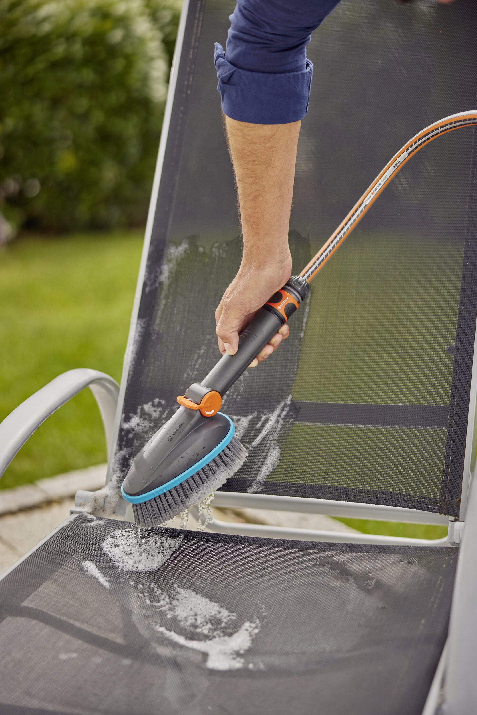 Osoba czyści szczotką krzesło ogrodowe na zewnątrz. Piana pokrywa siedzisko krzesła.