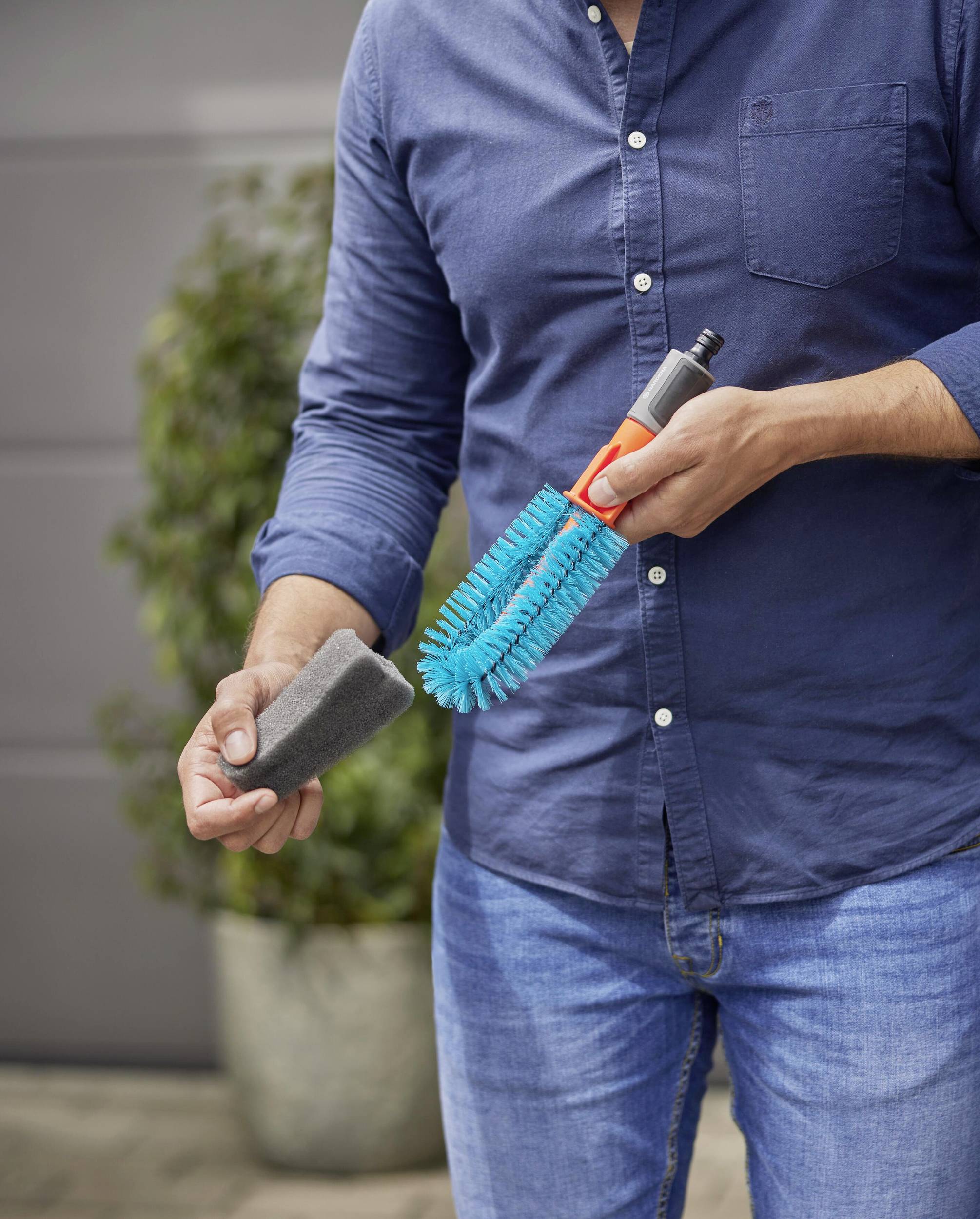 Osoba trzyma szczotkę do mycia samochodu i gąbkę w rękach, gotowa do czyszczenia. Tło jest rozmyte, a fokus skierowany na narzędziach.