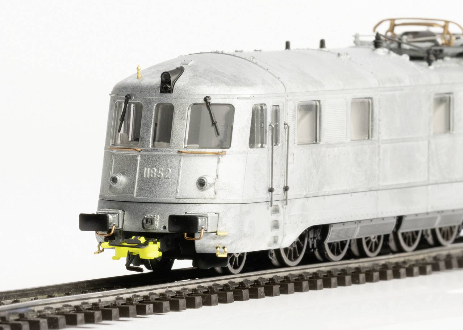 Srebrna modelowa lokomotywa elektryczna na torach, z dokładnie odwzorowanymi oknami i kołami, prezentuje widok od przodu z zderzakami.