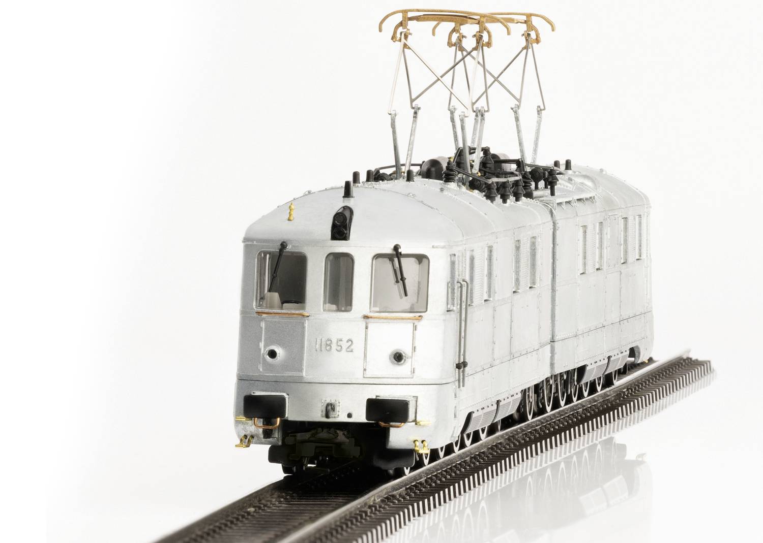 Srebrny pociąg modelowy o numerze '1852' stojący na torach. Pociąg posiada elektryczną sieć trakcyjną i jest wykonany z dużą dbałością o szczegóły.