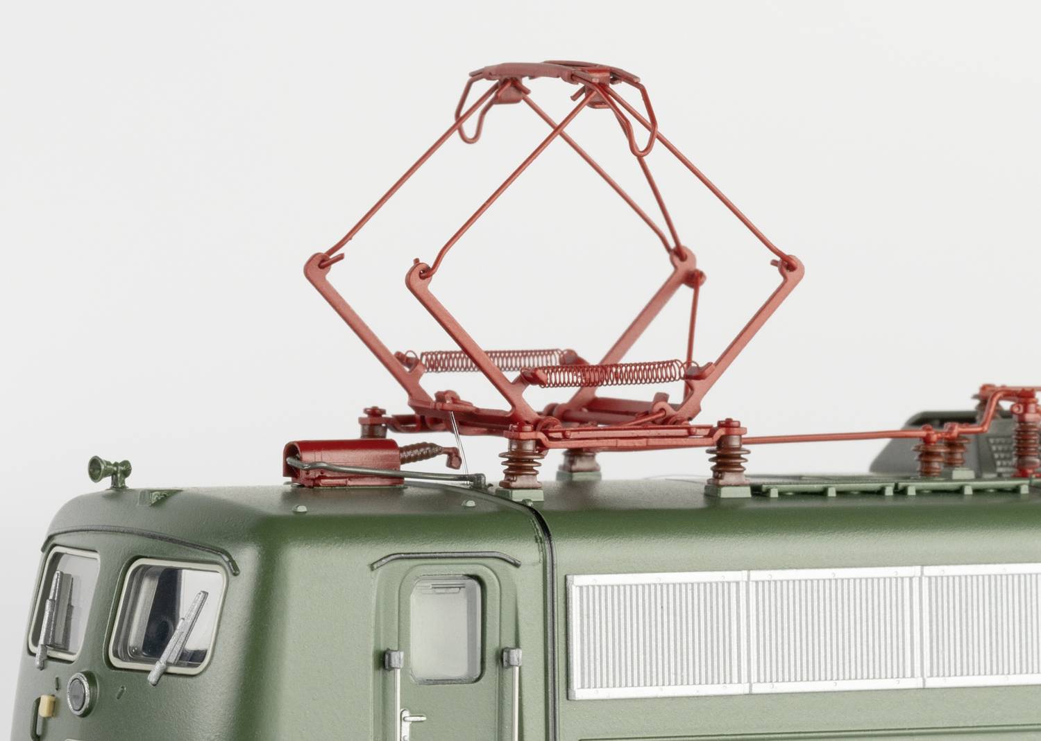 Zbliżenie zielonego modelu lokomotywy z dokładnie odwzorowanym czerwonym pantografem na dachu, na białym tle.