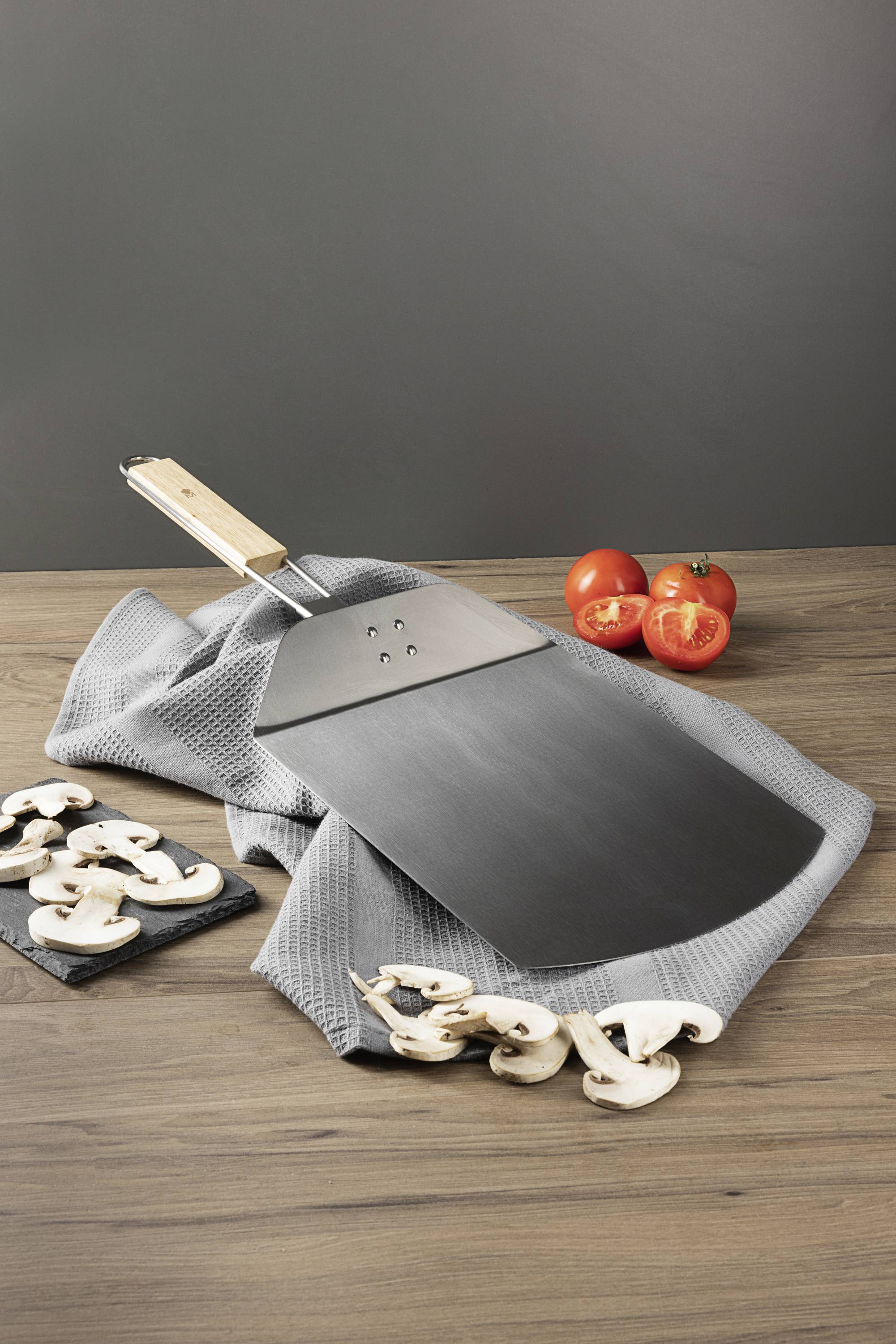 Metalowa łopatka do pizzy na szarym ręczniku, otoczona pokrojonymi pieczarkami i trzema pomidorami na drewnianym stole.