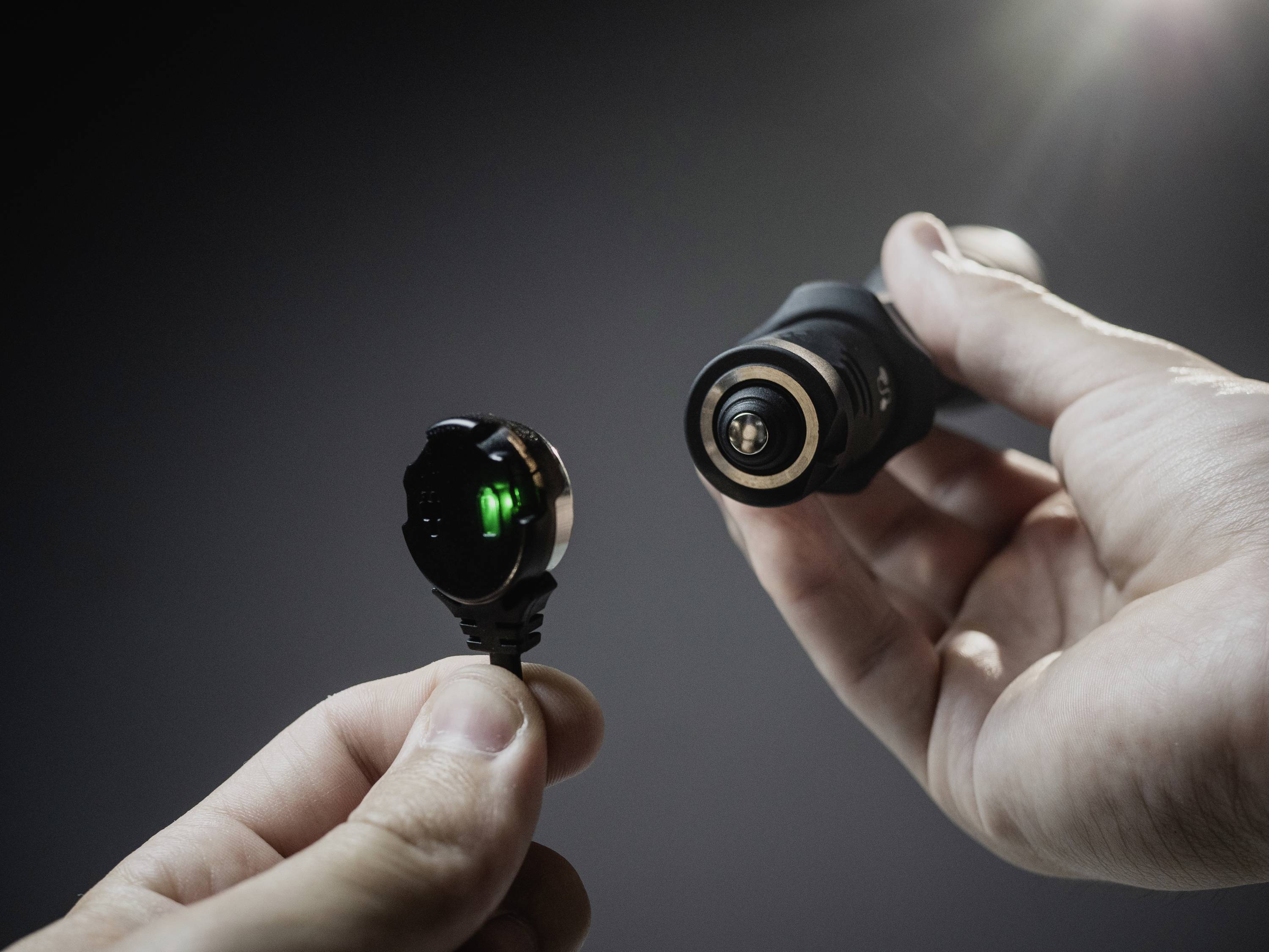 Dwie ręce trzymają wtyki magnetyczne blisko siebie. Jeden wtyk świeci się na zielono, co wskazuje na połączenie lub funkcję.