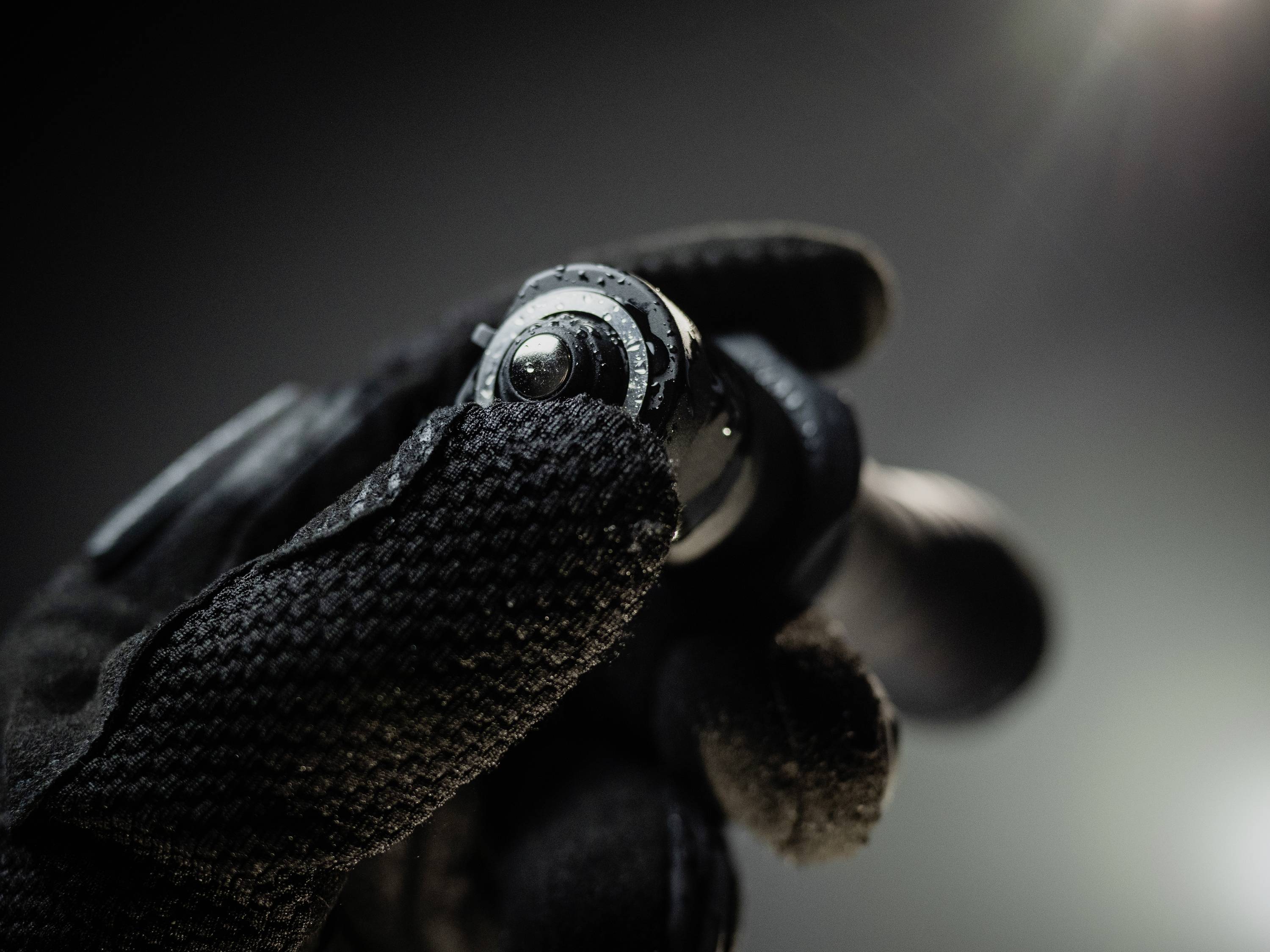 Dłoń w czarnej rękawiczce trzyma małą latarkę. Otoczenie jest ciemne, a latarka jest włączona.