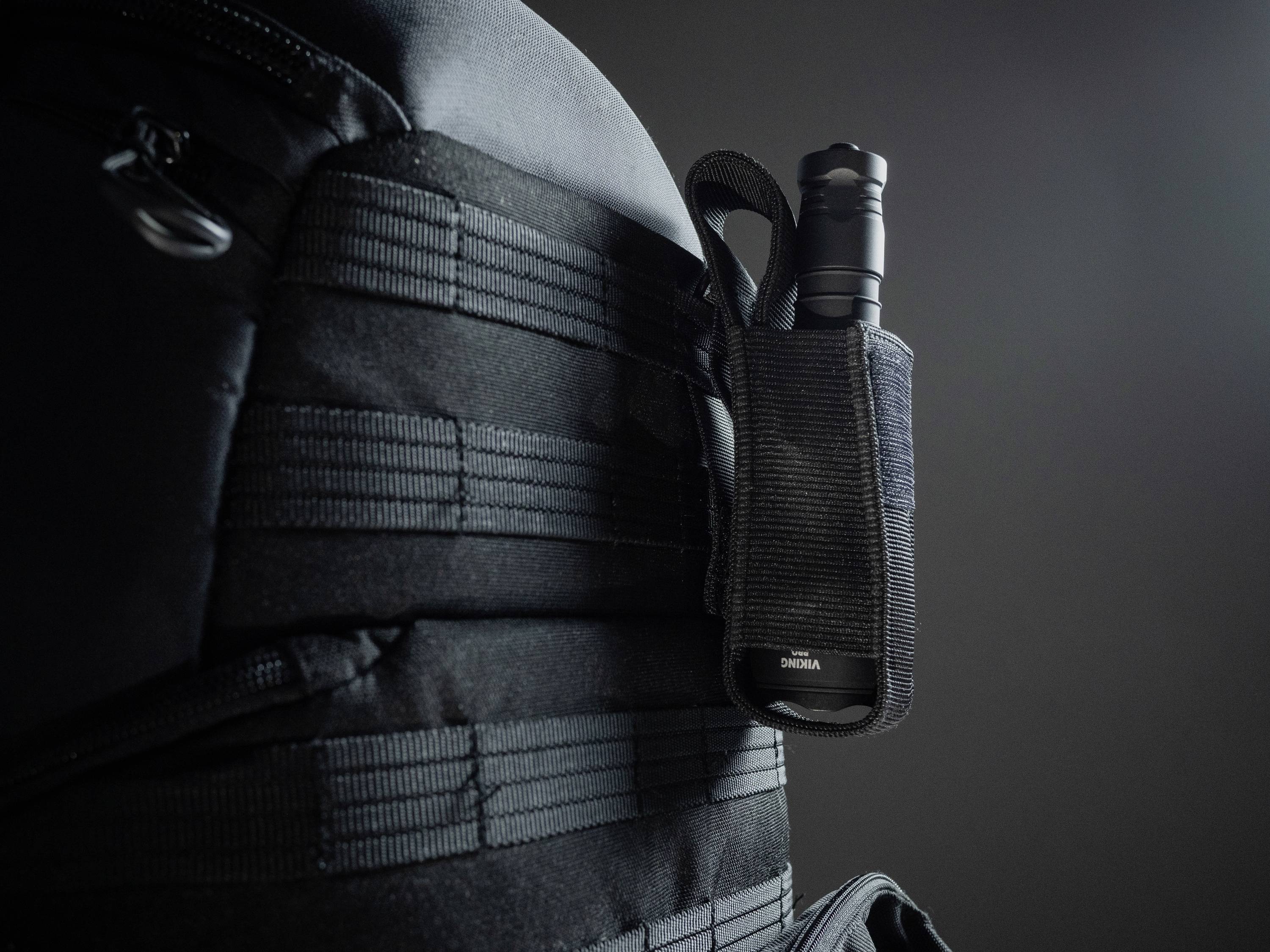 Czarny plecak z latarką w uchwycie po jego boku, na ciemnym tle.