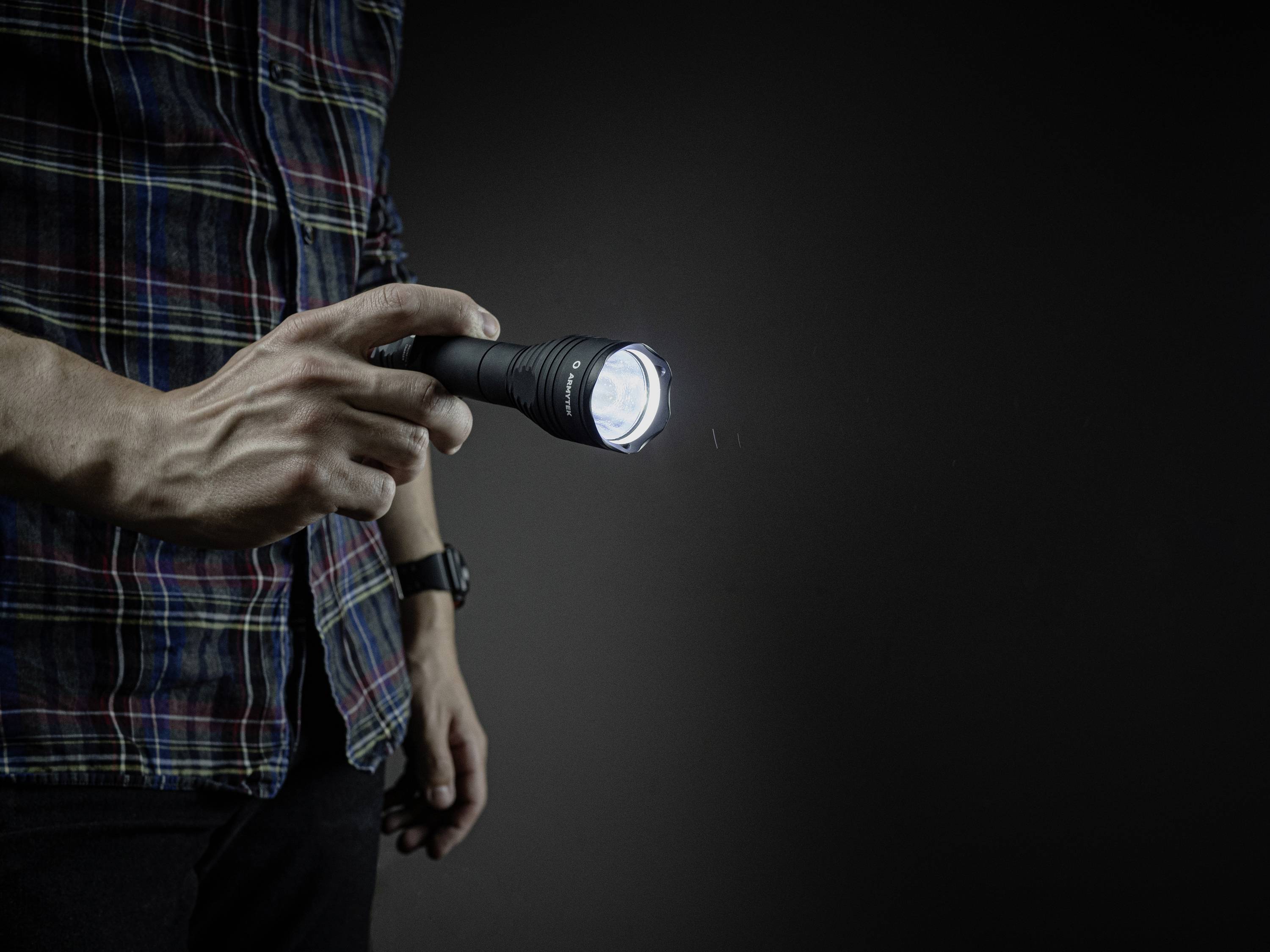 Osoba trzyma świecącą latarkę w słabo oświetlonym otoczeniu. Wiązka światła jest skierowana do przodu.