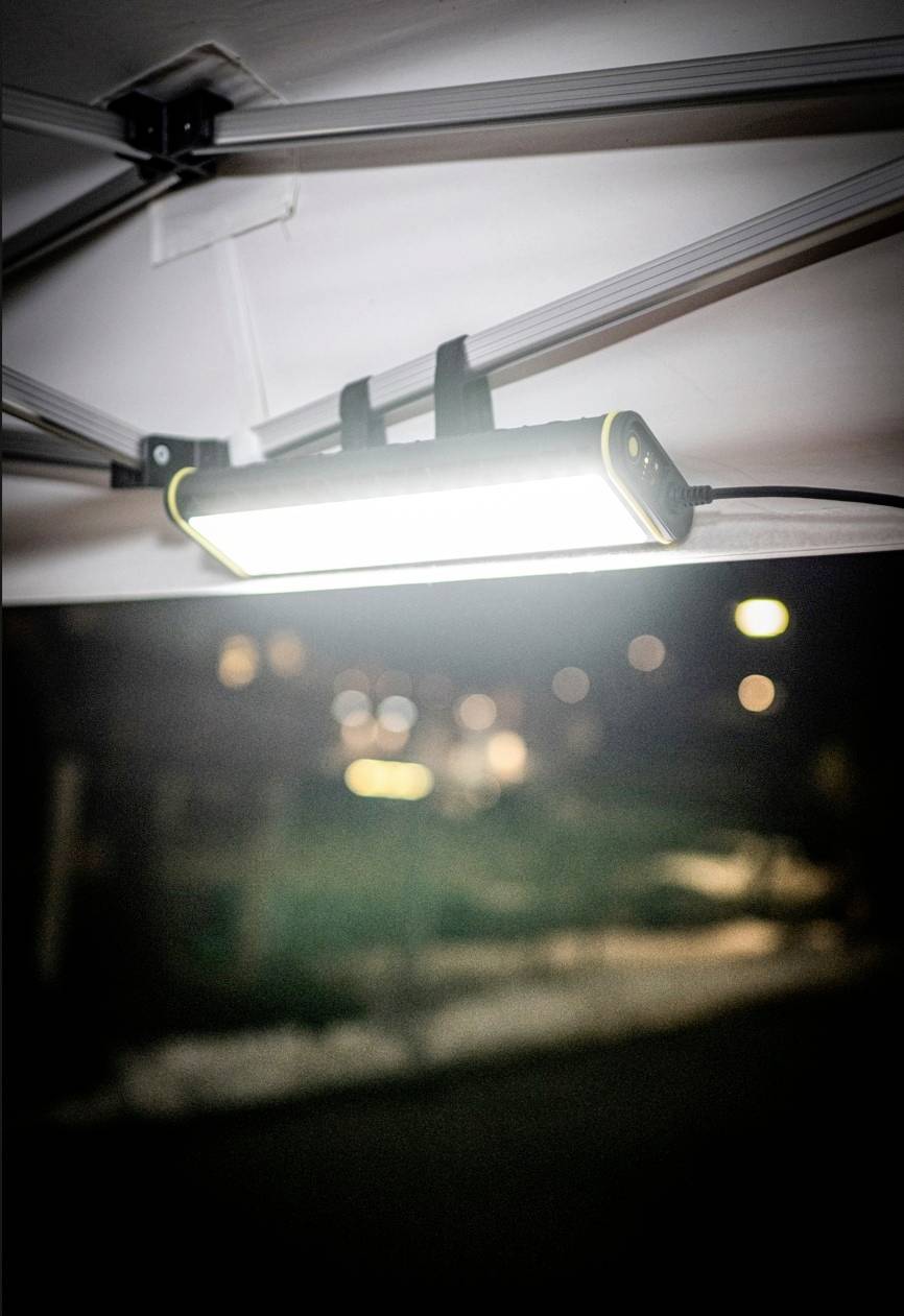 Jasne światło LED zamontowane na suficie oświetla nocną przestrzeń na zewnątrz. Rozmyty tło z drzewami i światłami.