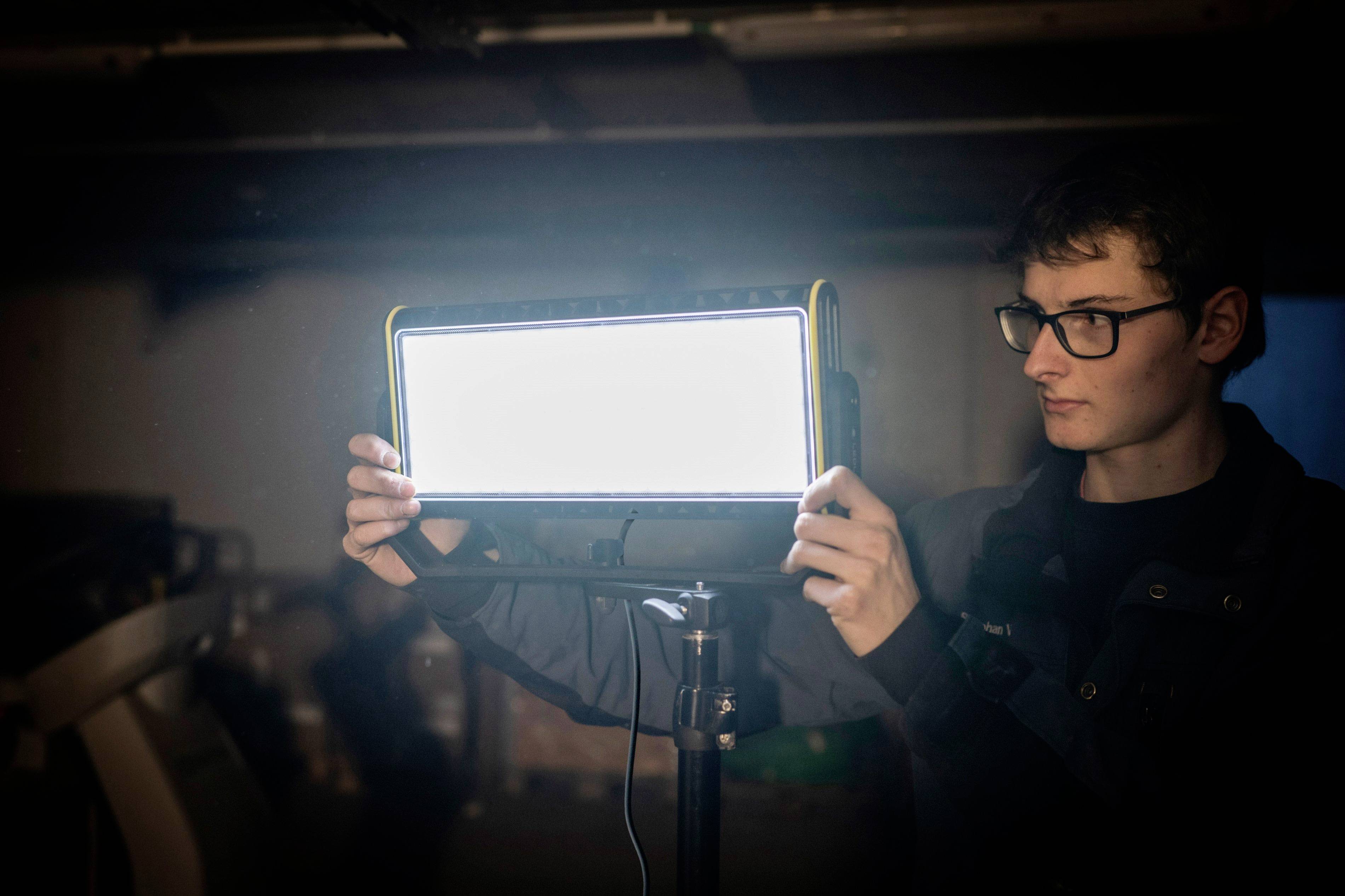 Osoba ustawia jasne światło studyjne w zaciemnionym pomieszczeniu.