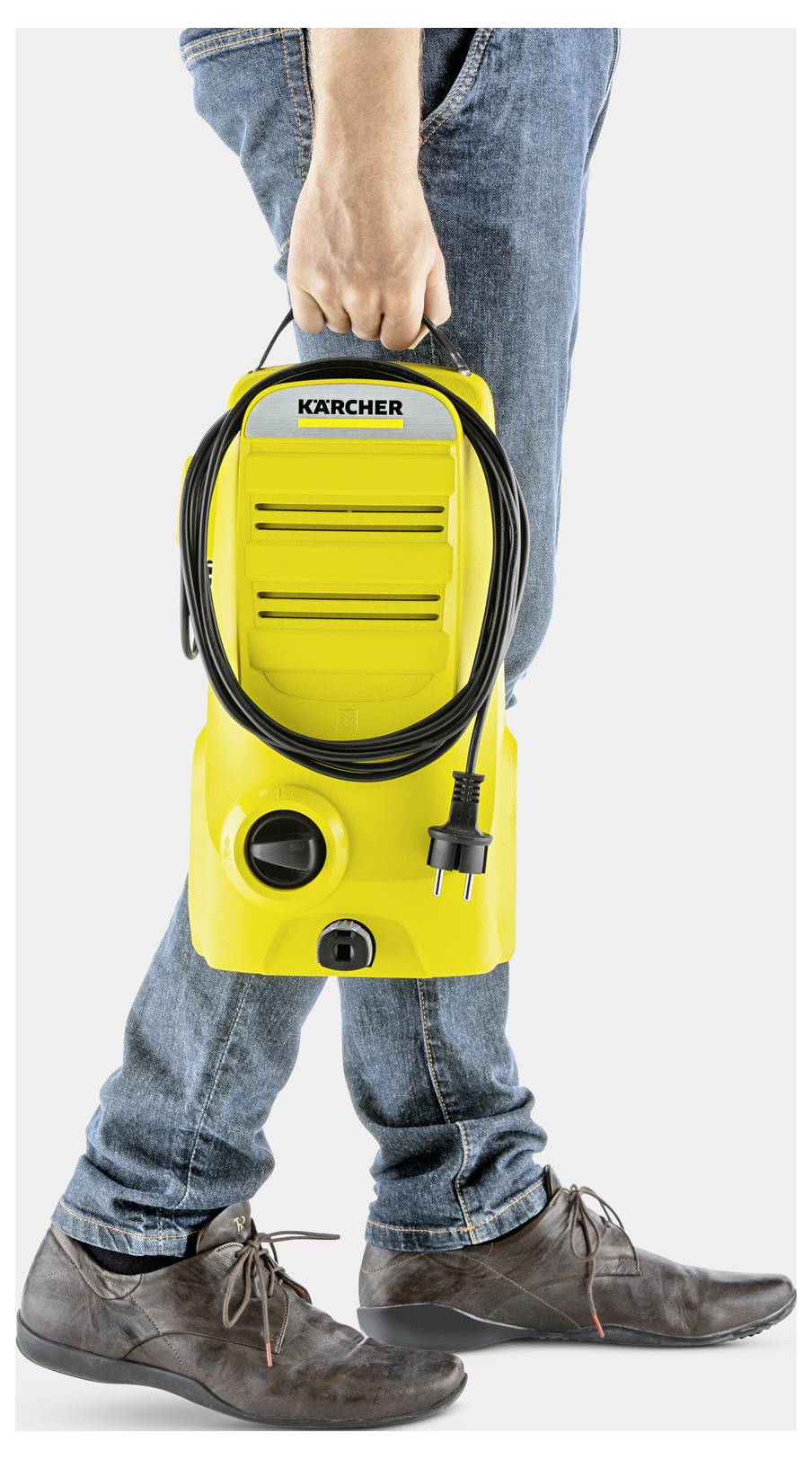 Osoba niesie żółtą myjkę ciśnieniową Kärcher uchwytem, demonstrując jej przenośność. Przewód zasilający jest starannie zwinięty wokół urządzenia.
