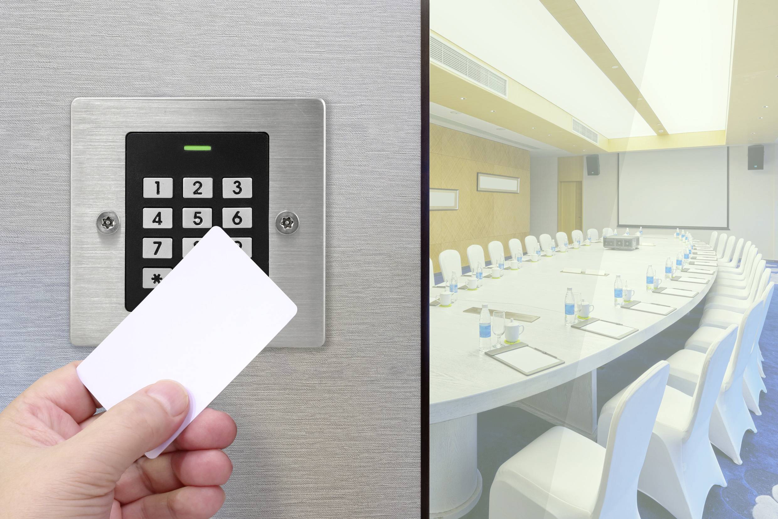 Ręka trzymająca kartę dostępu przed panelem sterującym obok pustej, nowoczesnej sali konferencyjnej z dużym owalnym stołem i białymi krzesłami.