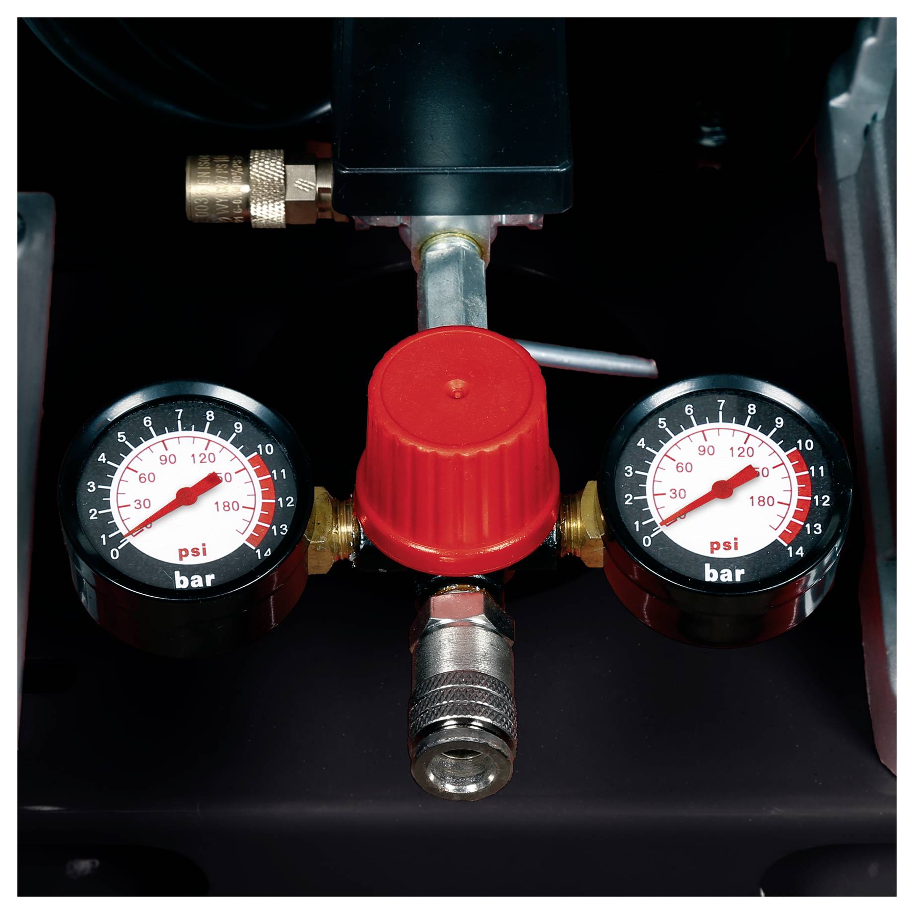 Zbliżenie na regulator ciśnienia powietrza z czerwoną pokrętłem regulacyjnym i dwoma manometrami pokazującymi ciśnienie w psi i bar.