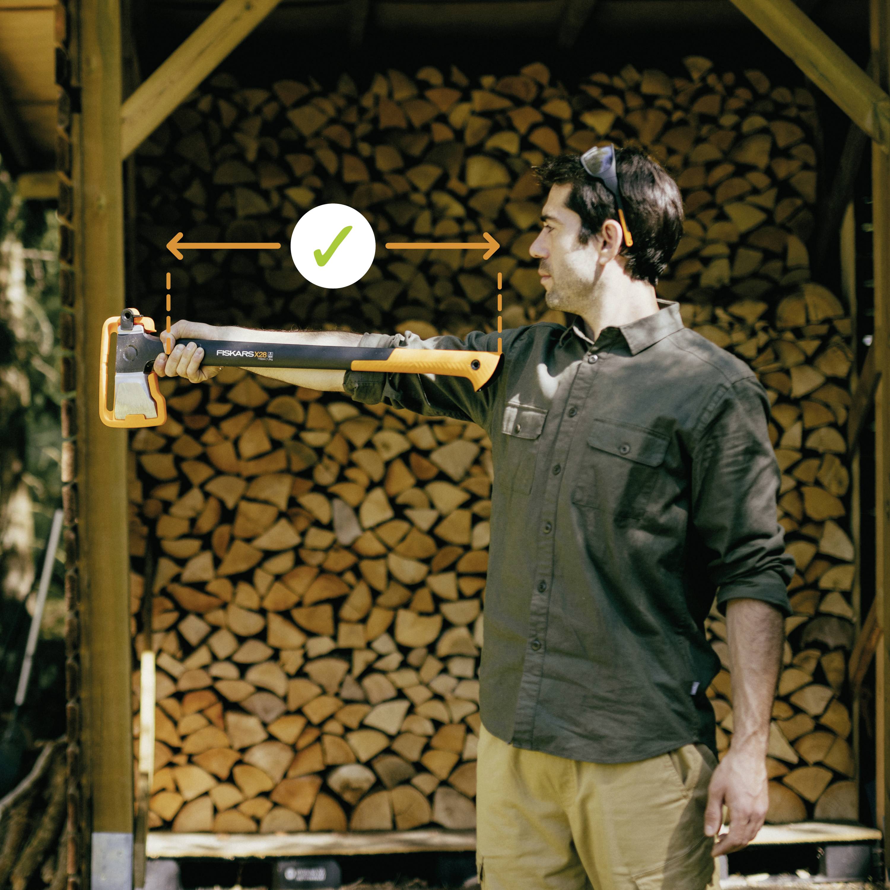 Mężczyzna stoi przed ułożonym drewnem i trzyma w ręku siekierę. Znacznik ze strzałkami wskazuje równowagę siekiery.