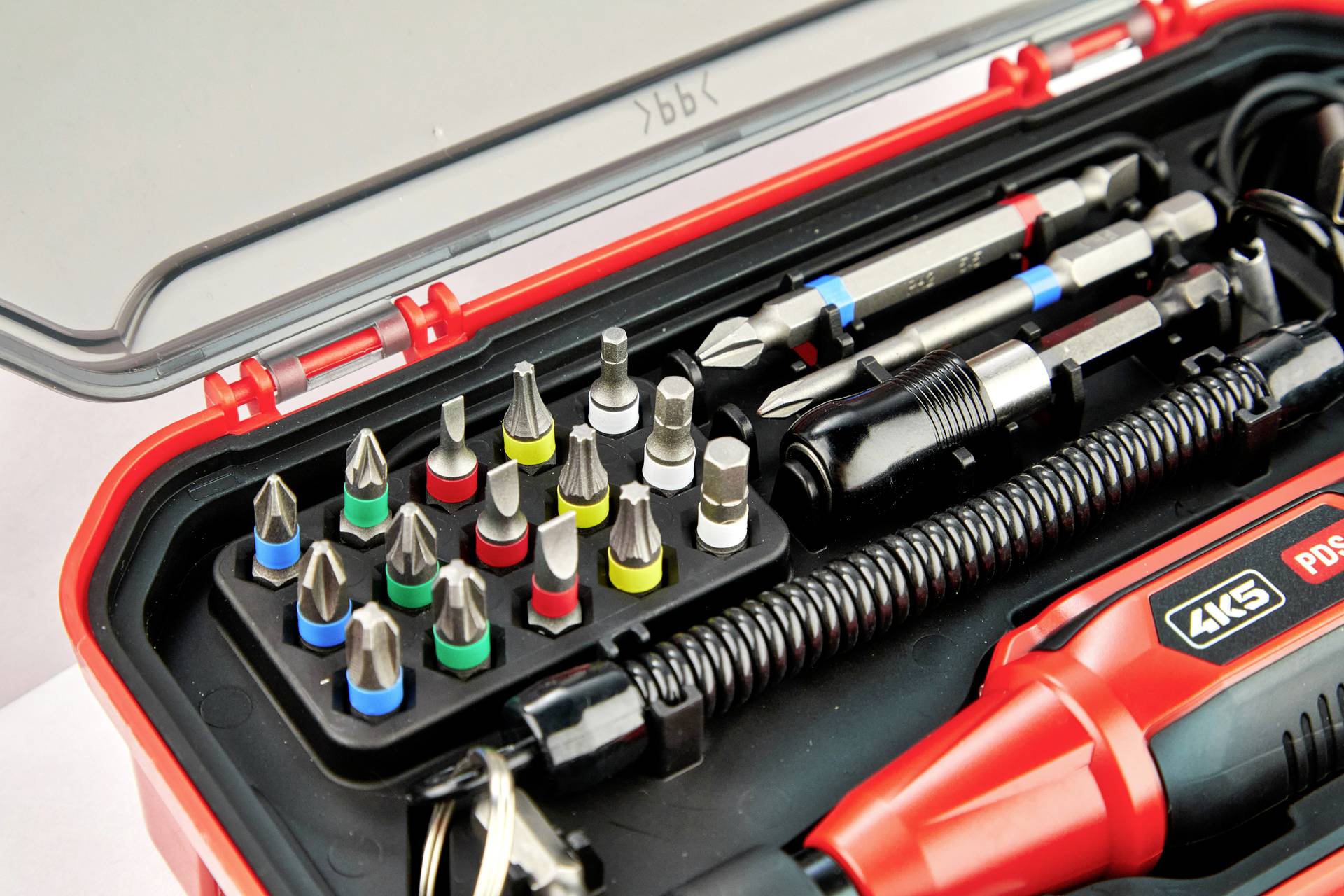Czerwona skrzynka narzędziowa z różnymi końcówkami wkrętakowymi w kolorowych uchwytach oraz elektrycznym wkrętakiem.