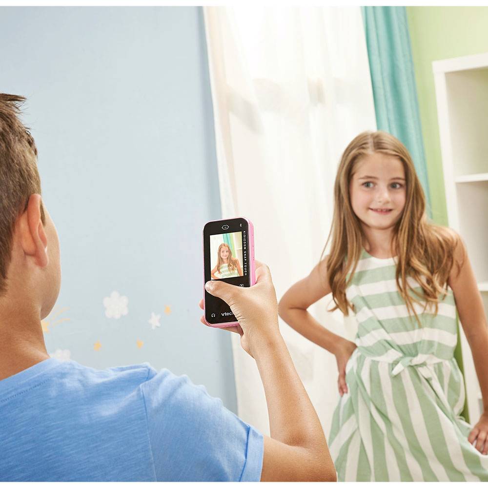 Chłopiec fotografuje uśmiechnięte dziewczę w pomieszczeniu. Dziewczyna ma na sobie sukienkę w paski i pozuje do zdjęcia.