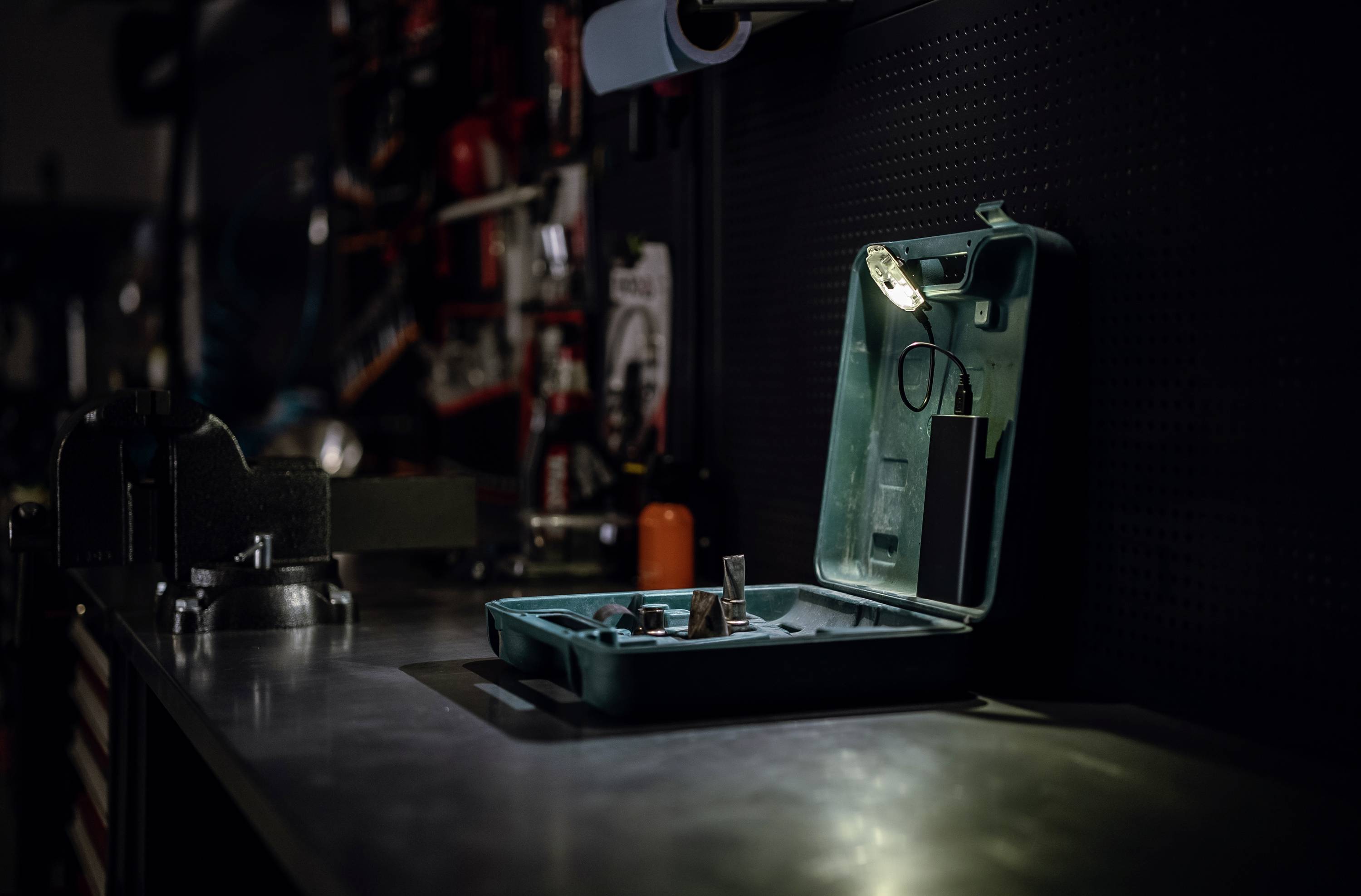 Otwarty zestaw narzędzi na stole warsztatowym w warsztacie. W tle narzędzia wiszące na ścianie. Całościowy widok warsztatu.