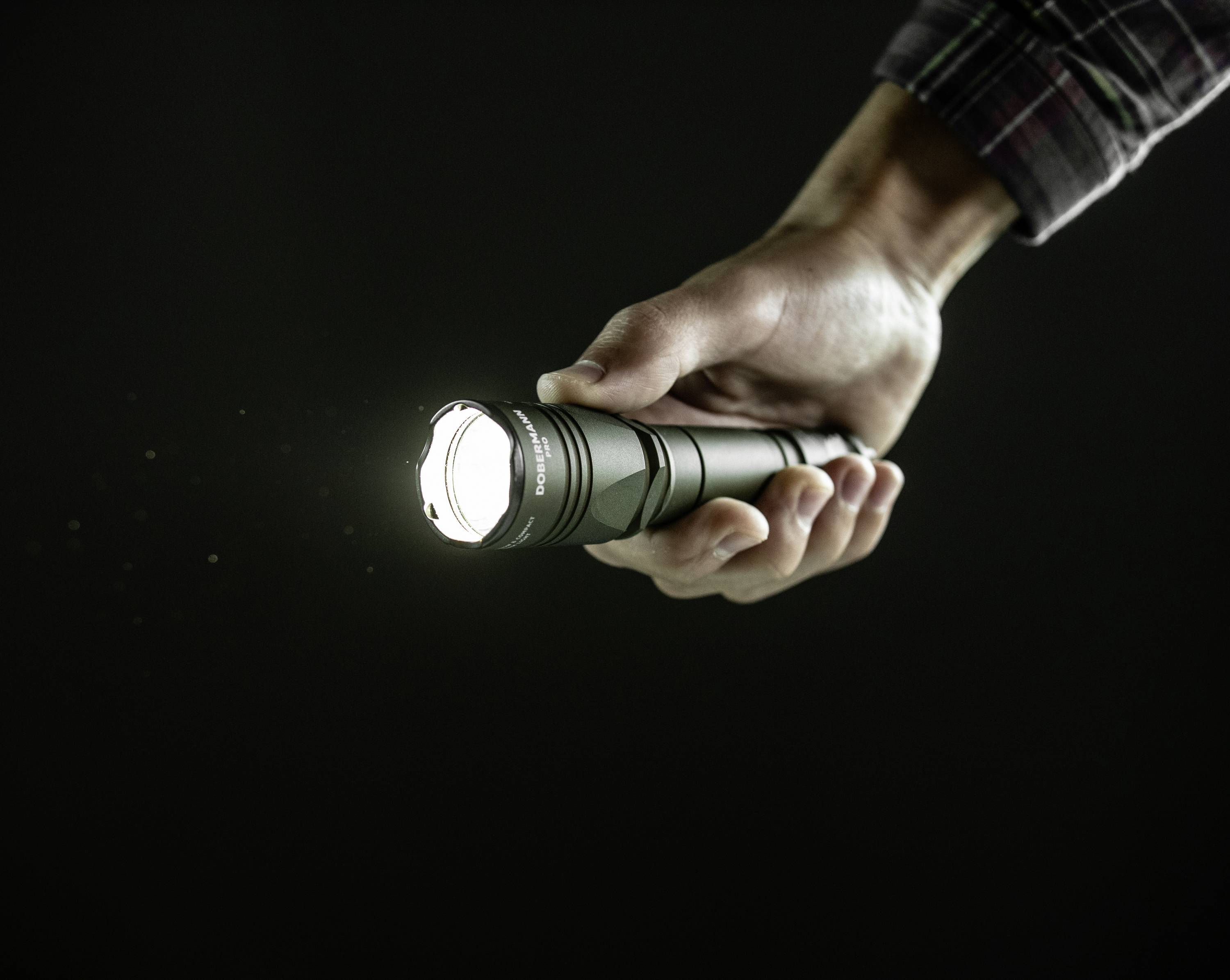 Dłoń trzyma włączoną latarkę, która świeci w ciemnym pomieszczeniu.