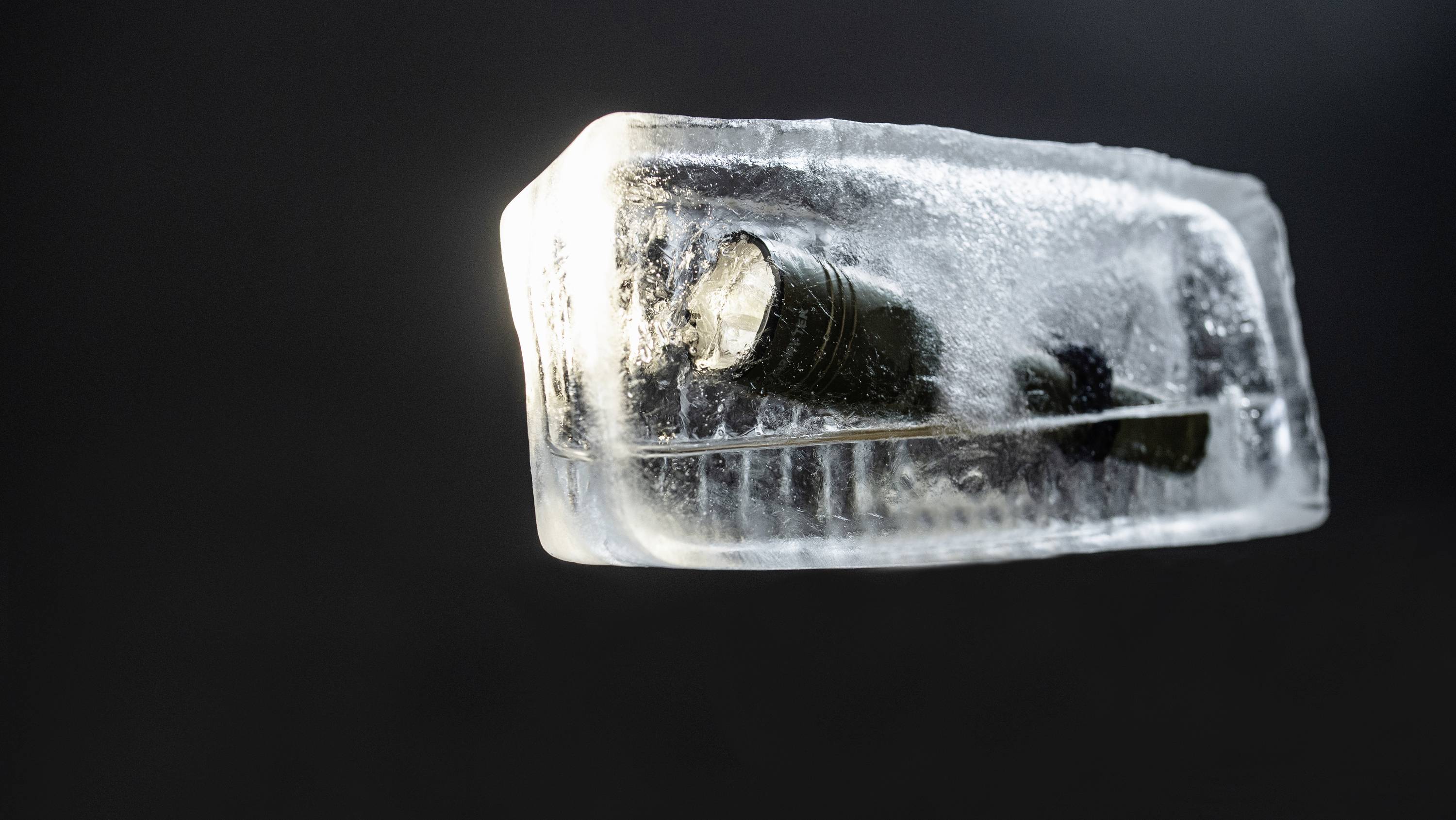 Latarka zamrożona w bloku lodu, na ciemnym tle.