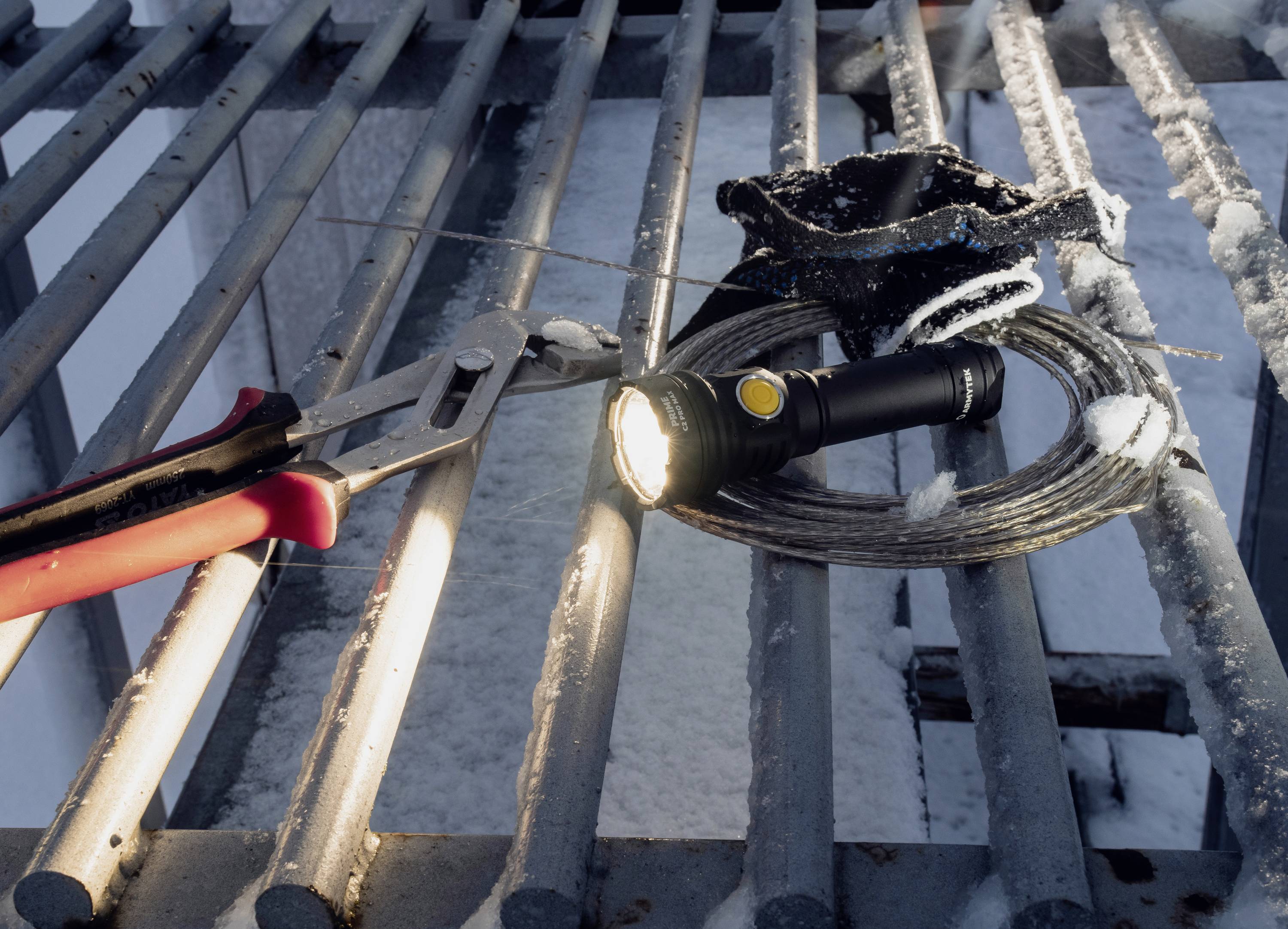 Latarka świeci na kracie stalowej, obok leży klucz francuski i wiązka drutu.