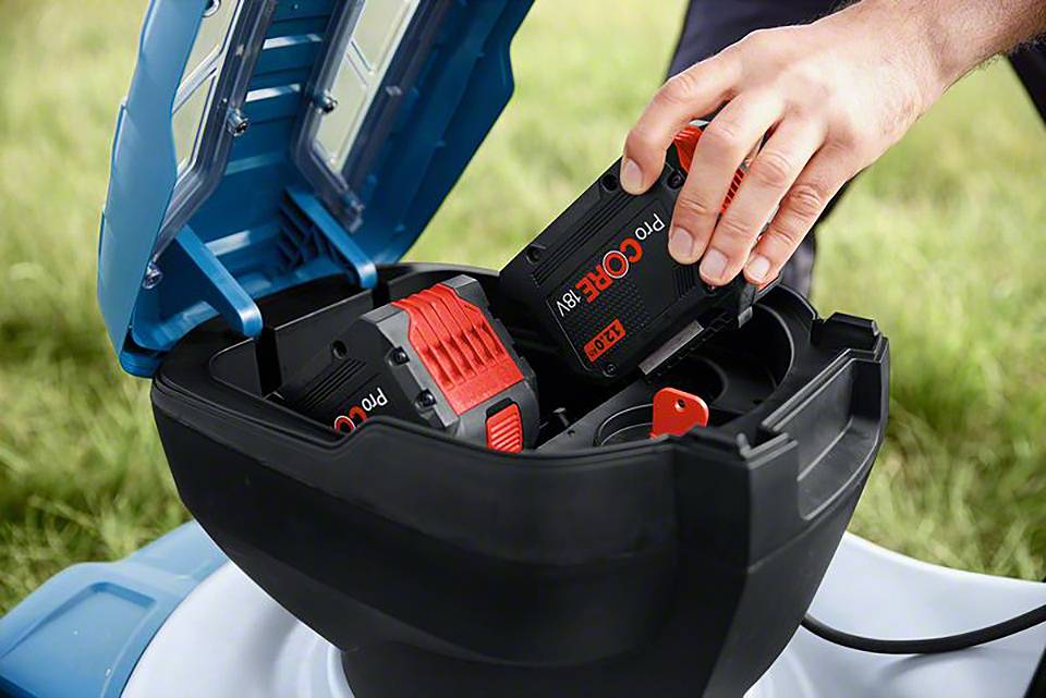 Ręka wkłada akumulator do zasilanego bateryjnie urządzenia ogrodowego. Akumulator jest czarny z czerwonymi akcentami i nosi napis 'ProCORE'.