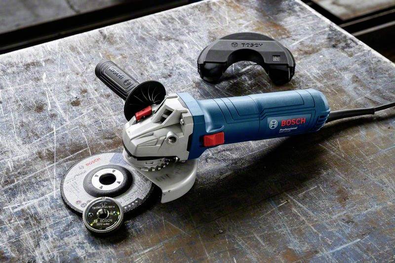 Niebieska szlifierka kątowa marki 'Bosch' leży na metalowym stole, otoczona tarczą szlifierską i osłoną ochronną.