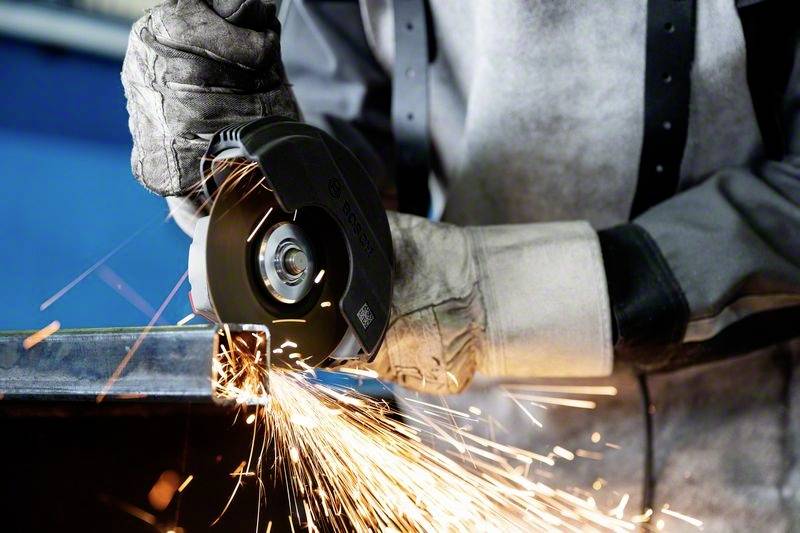 Osoba tnie metal piłą tarczową, lecą iskry. Nosi odzież ochronną.