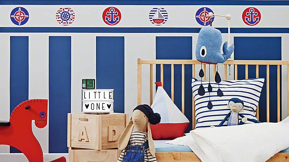 Pokój dziecięcy w stylu morskim. Łóżeczko dziecięce otoczone jest zabawkami i dekoracjami, w tym czerwonym koniem na biegunach.