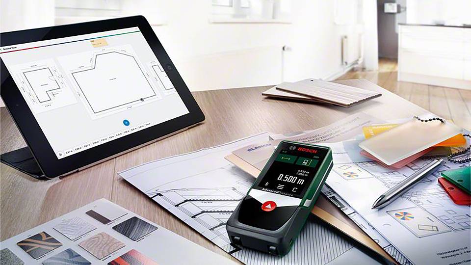Tablet z planem przestrzennym i laserowym miernikiem odległości na biurku pełnym planów budowlanych i próbek kolorów w biurze.