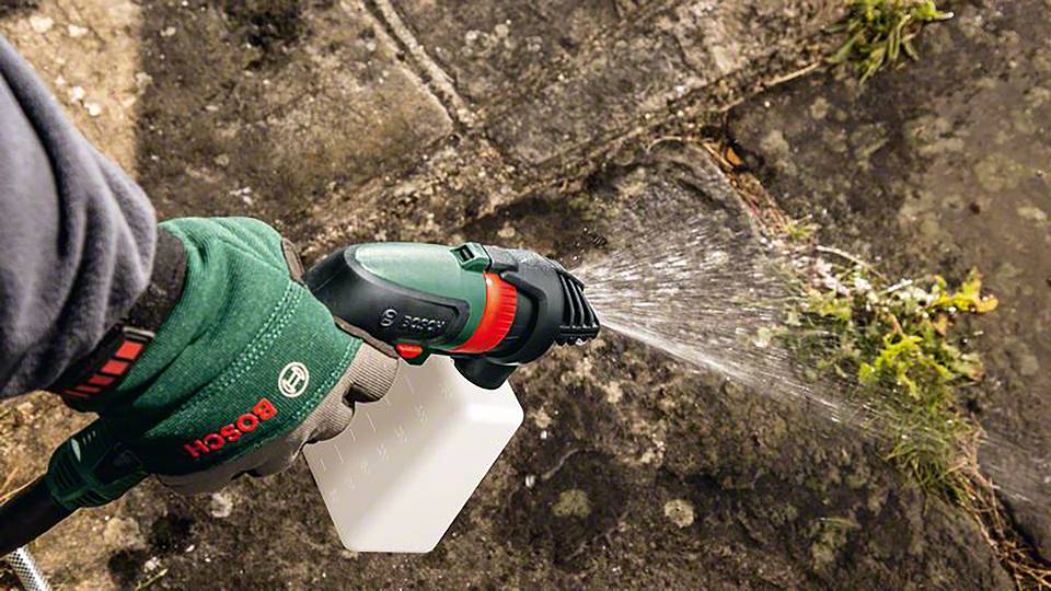 Osoba używa myjki wysokociśnieniowej do spryskiwania pokrytych mchem kostek brukowych, aby je wyczyścić.