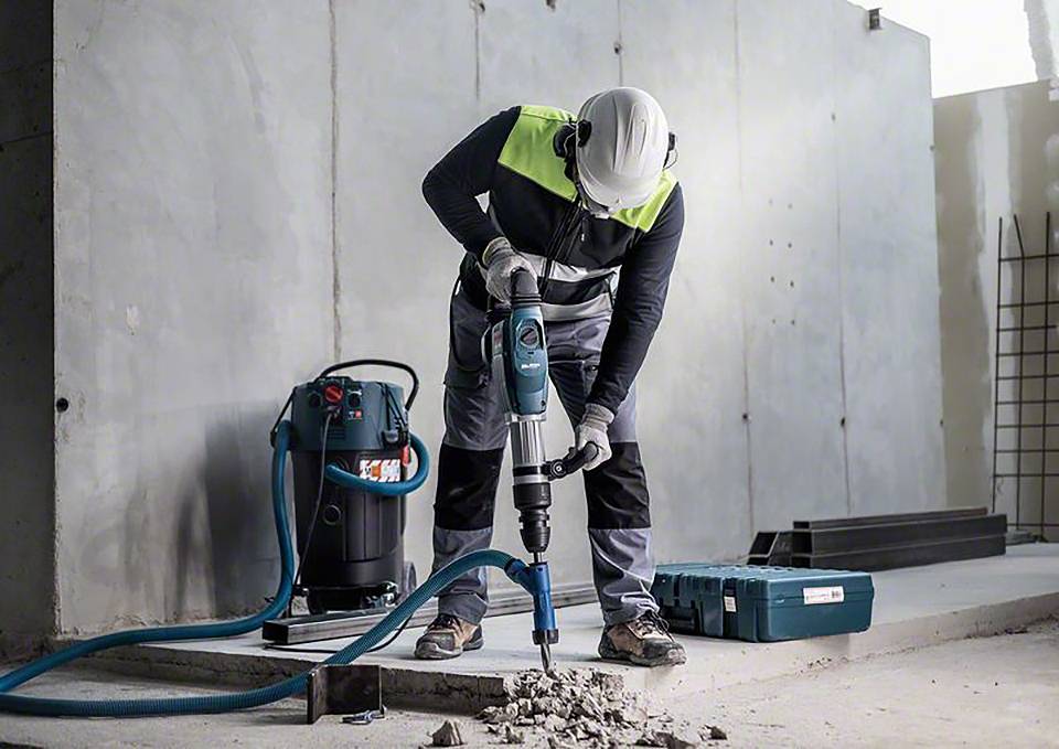 Robotnik w odzieży ochronnej używa elektrycznego młotowiertarki do rozbijania betonu na placu budowy.