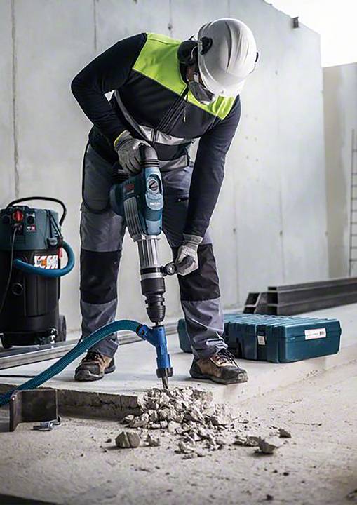 'Robotnik w odzieży ochronnej obsługuje młot udarowy na placu budowy.'