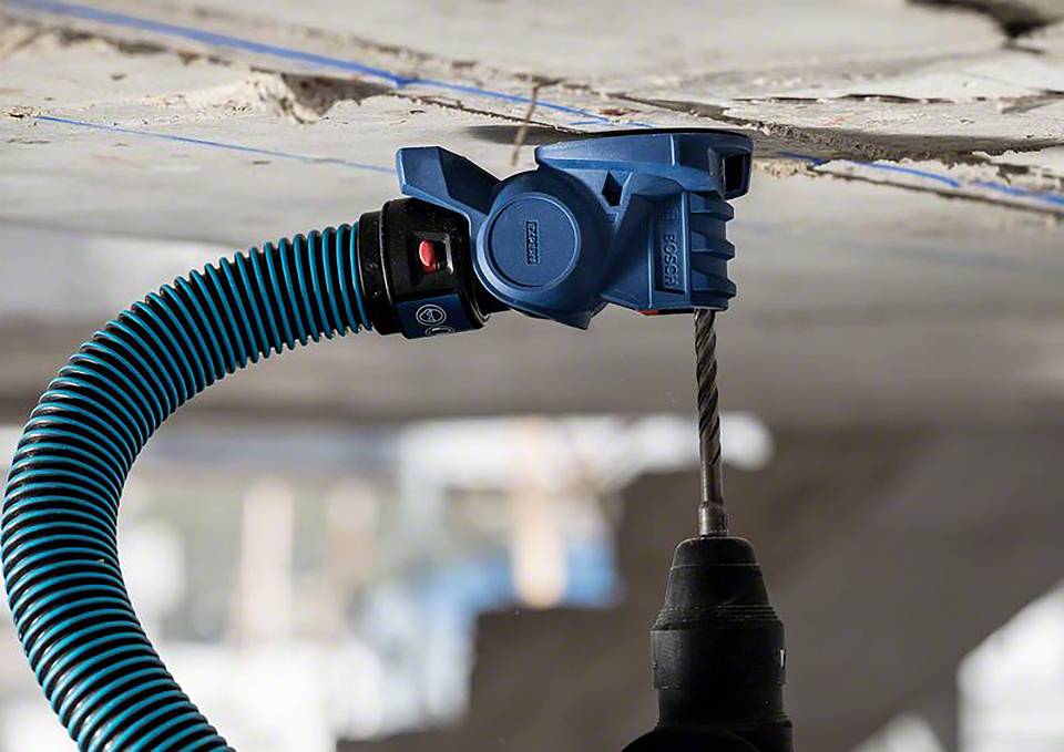 Niebieski adapter odkurzacza na wiertarce usuwa pył z otworu w suficie.