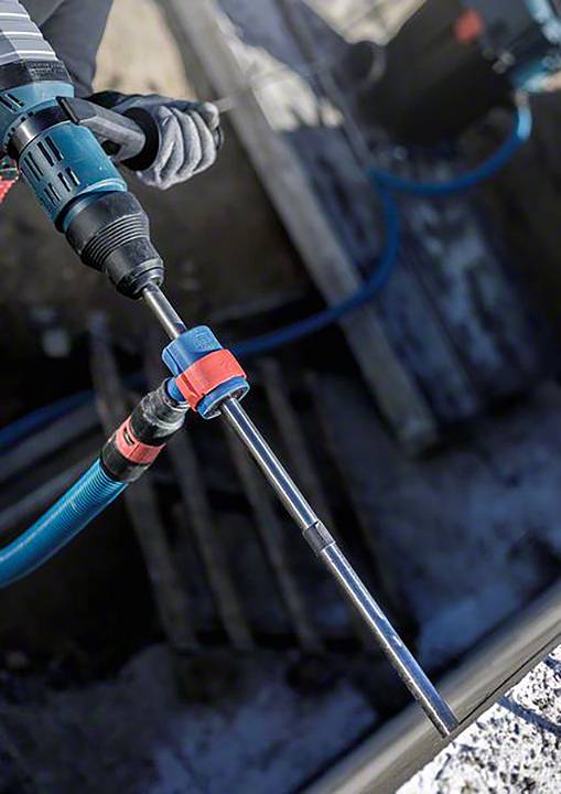 Osoba obsługuje młot udarowy na placu budowy. Wiertło jest wyposażone w długie dłuto, przeznaczone do rozbijania betonu.