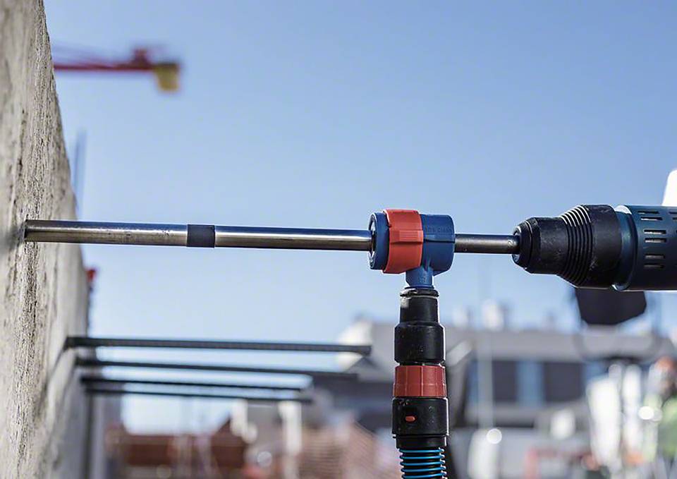 Wiercenie przez ścianę betonową. W tle rusztowania budowlane i dźwig. Czynności na placu budowy.