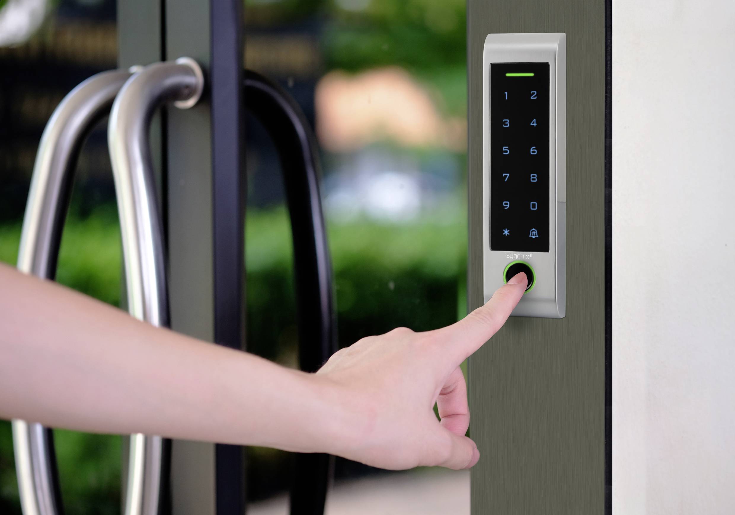 Ręka naciska klawisze elektronicznego zamka numerycznego na szklanych drzwiach, aby uzyskać dostęp.