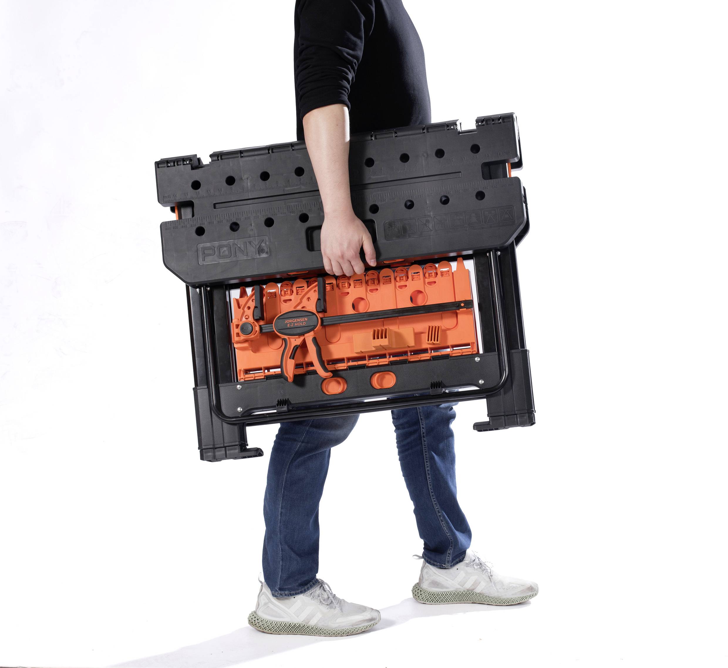 Osoba niesie czarną skrzynkę narzędziową z pomarańczową przegródką. Osoba ma na sobie dżinsy i białe buty.
