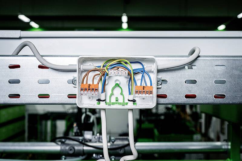 Otwarty rozdzielacz elektryczny z kolorowymi przewodami podłączonymi do różnych zacisków, zamontowany na szynie metalowej.