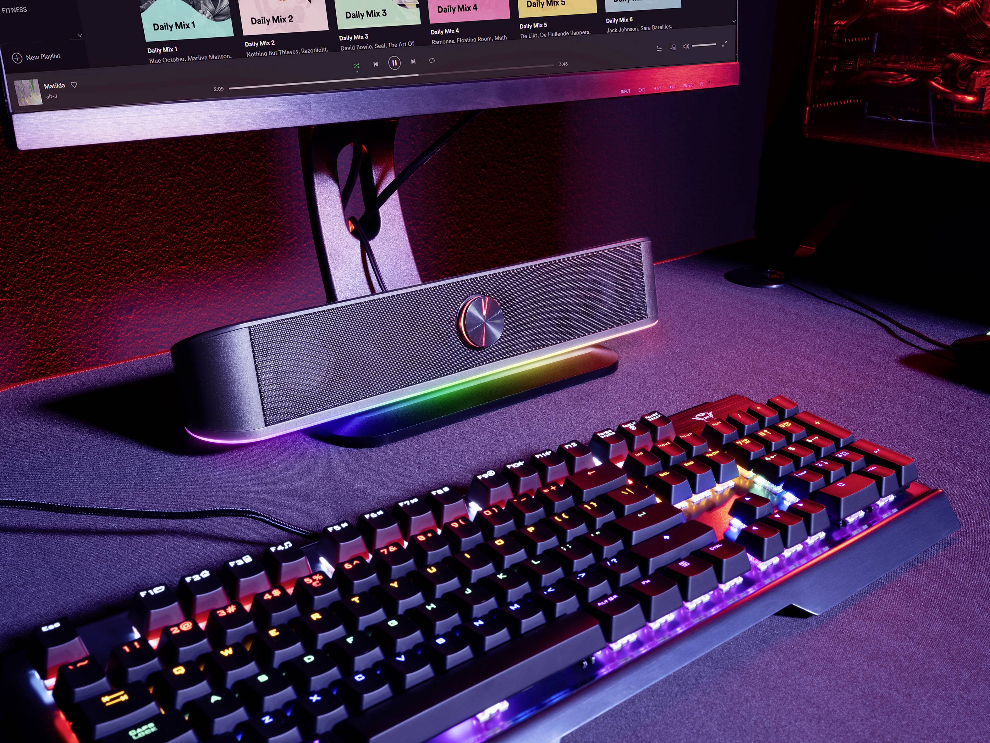 Podświetlony biurko gamingowe z klawiaturą, głośnikami i monitorem. Fokus na klawiaturze z podświetleniem RGB i eleganckiej aranżacji.