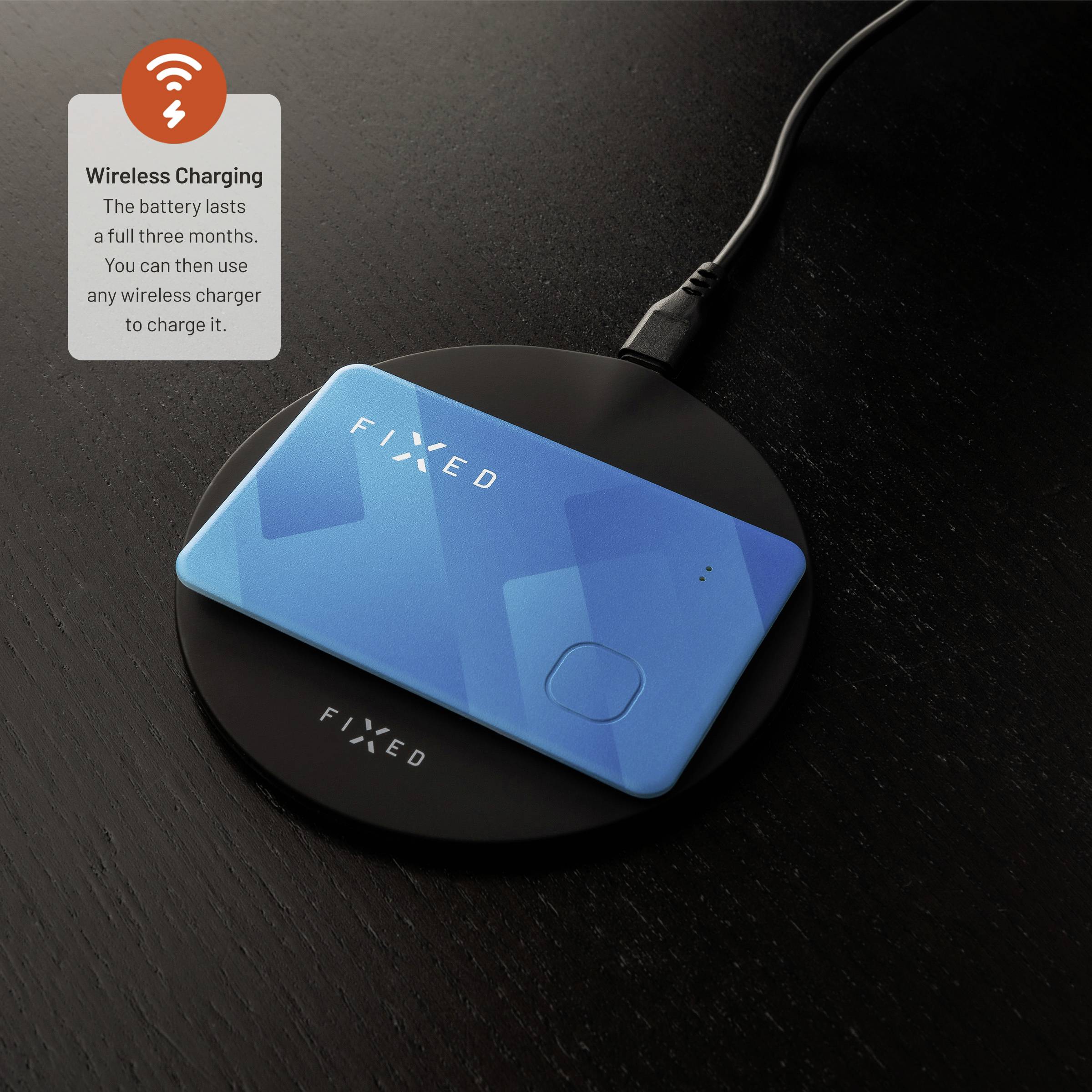 Niebieski bezprzewodowy tracker z logo 'FIXED' na czarnej stacji ładującej. Tekst: 'Ładowanie bezprzewodowe. Bateria wytrzymuje pełne trzy miesiące. Następnie możesz użyć dowolnej ładowarki bezprzewodowej, aby go naładować.'