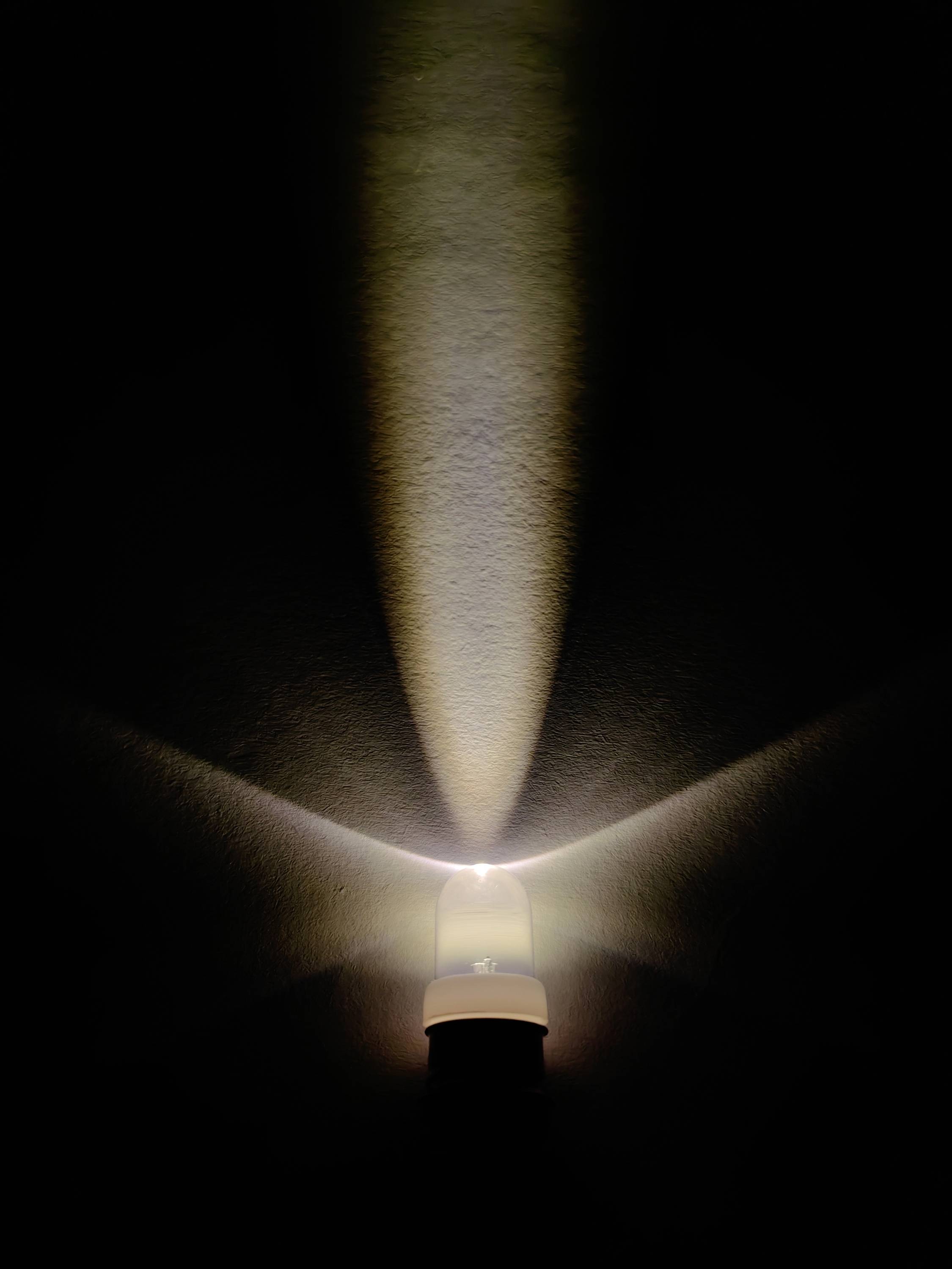 Żarówka świeci w ciemnym pokoju, tworząc promieniste wzory świetlne na ścianie.