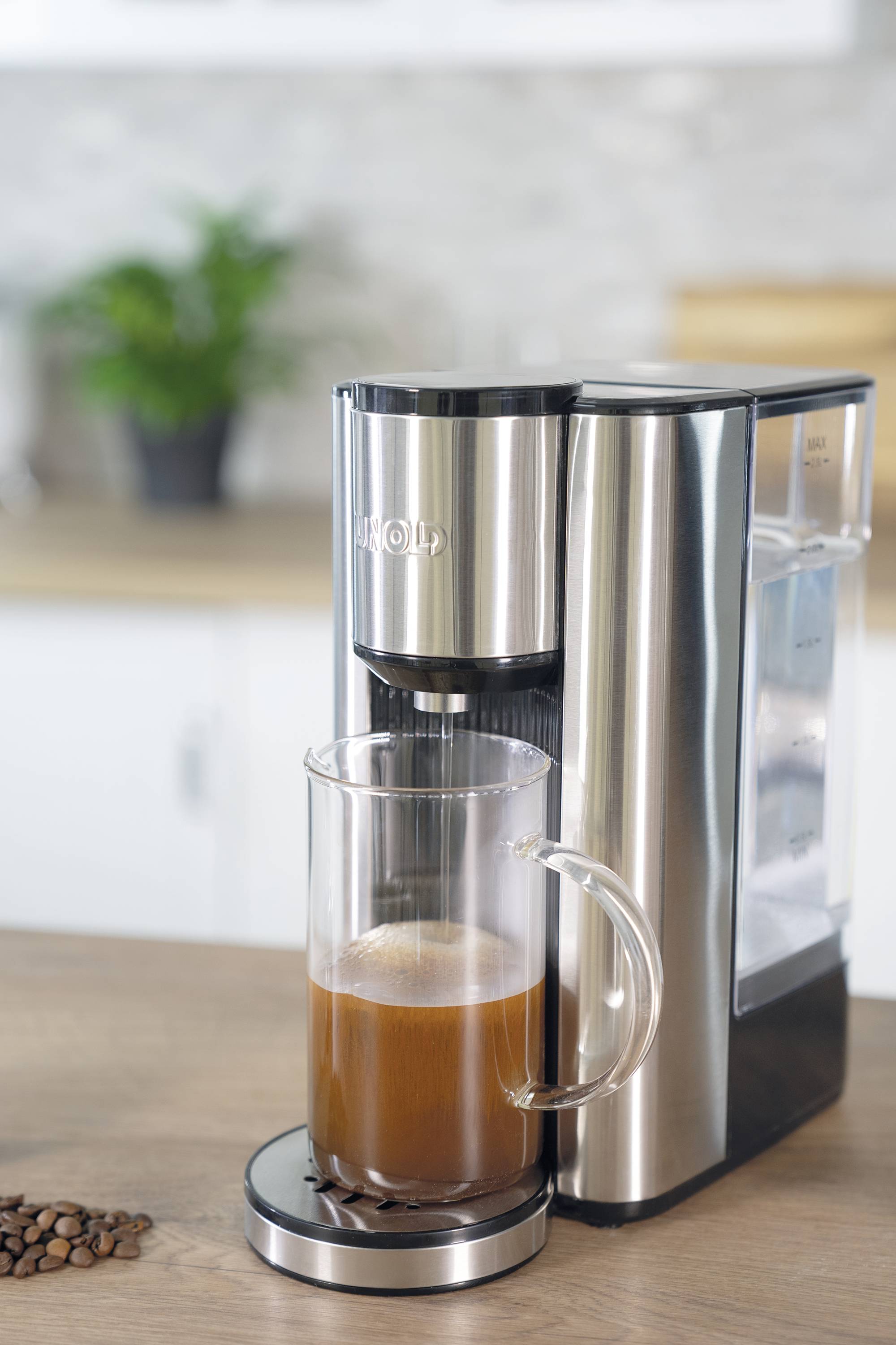 Na blacie kuchennym stoi srebrny ekspres do kawy, który parzy filiżankę kawy. W tle widać rozmyte elementy kuchni.