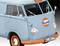Jasnobłękitny volkswagen bus z logo 'Gulf' oraz pomarańczowymi paskami i felgami stoi przed neutralnym tłem.