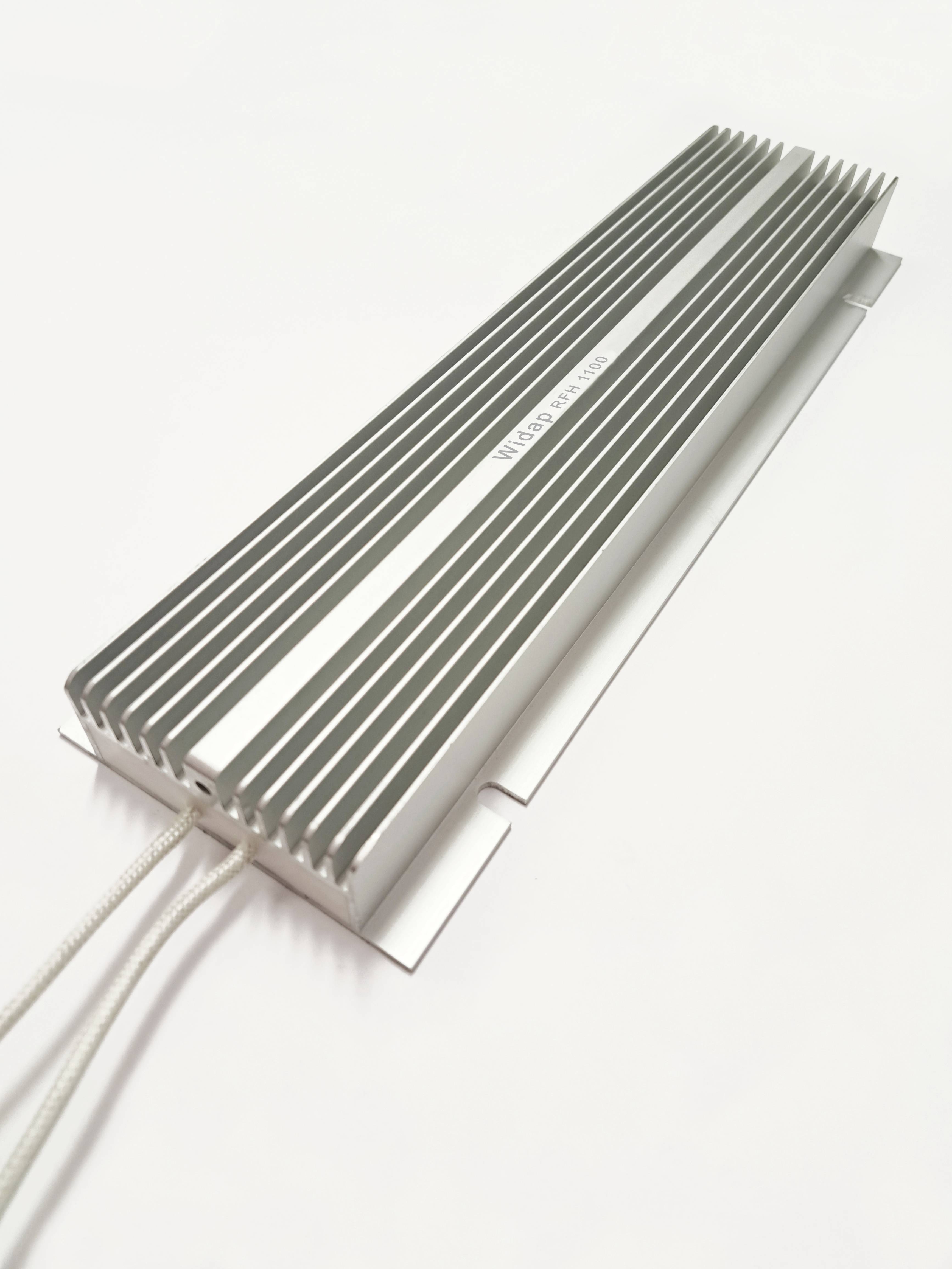 Metalowy radiator z podłużnymi żeberkami i kablami, leżący na białej powierzchni. Wydrukowany tekst: 'W160-300100'.