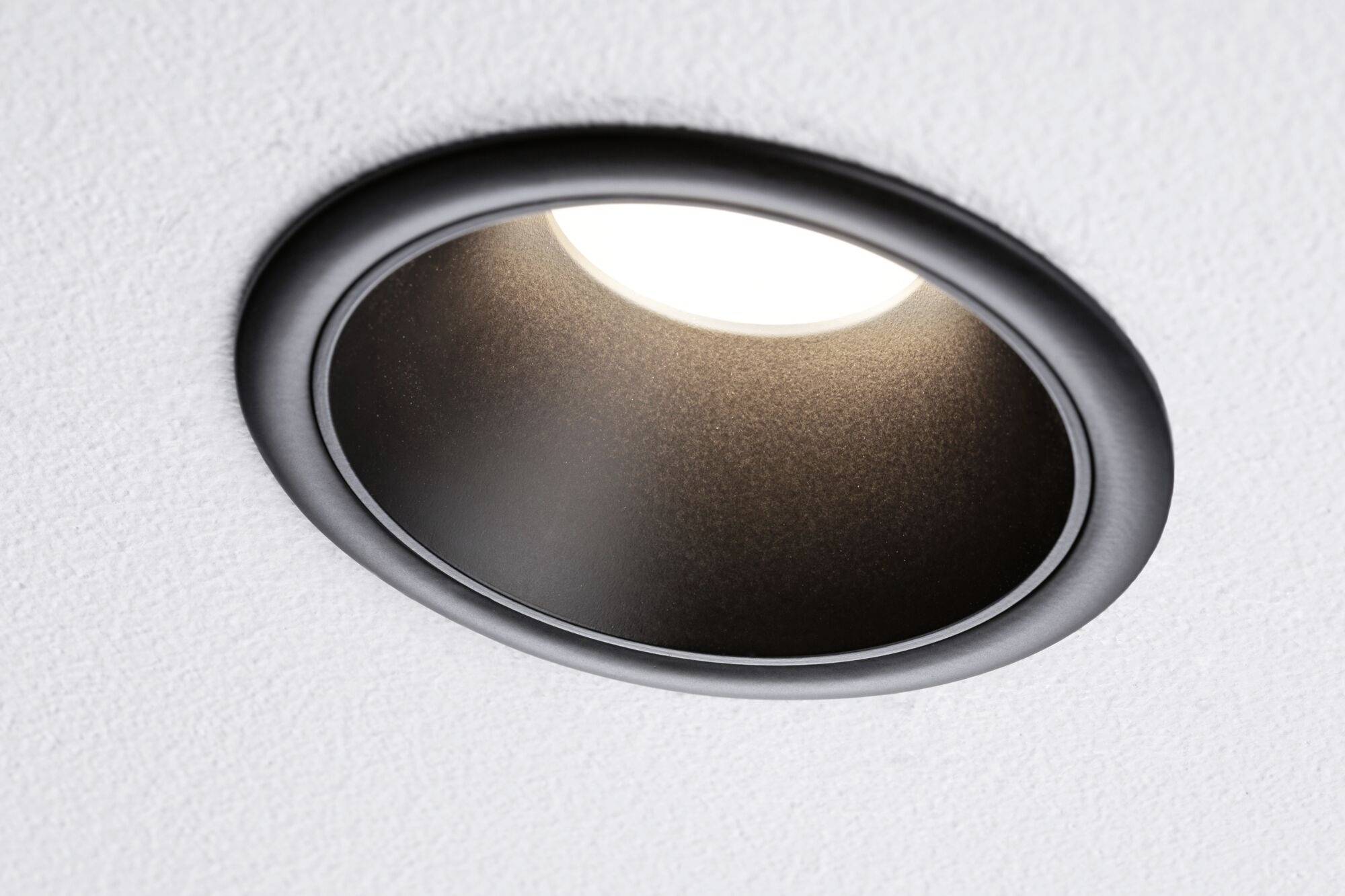 Okrągła, wpuszczona w sufit lampa sufitowa z czarną ramką świeci od góry w dół.
