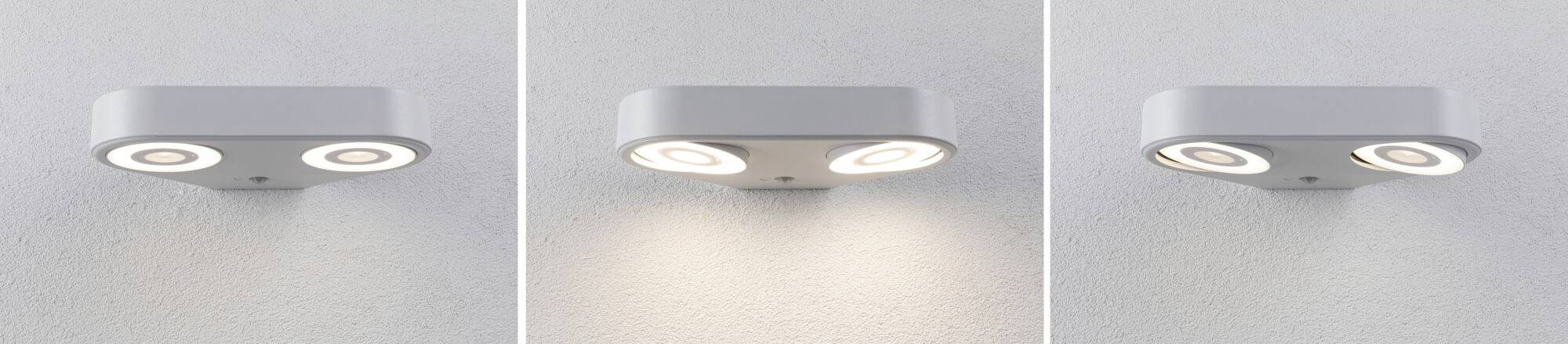 Trzy kinkiety w nowoczesnym stylu świecą na szarej ścianie. Lampa po lewej i prawej stronie rzucają wyraźne snopy światła, podczas gdy środkowa emituje miękkie, rozproszone światło.