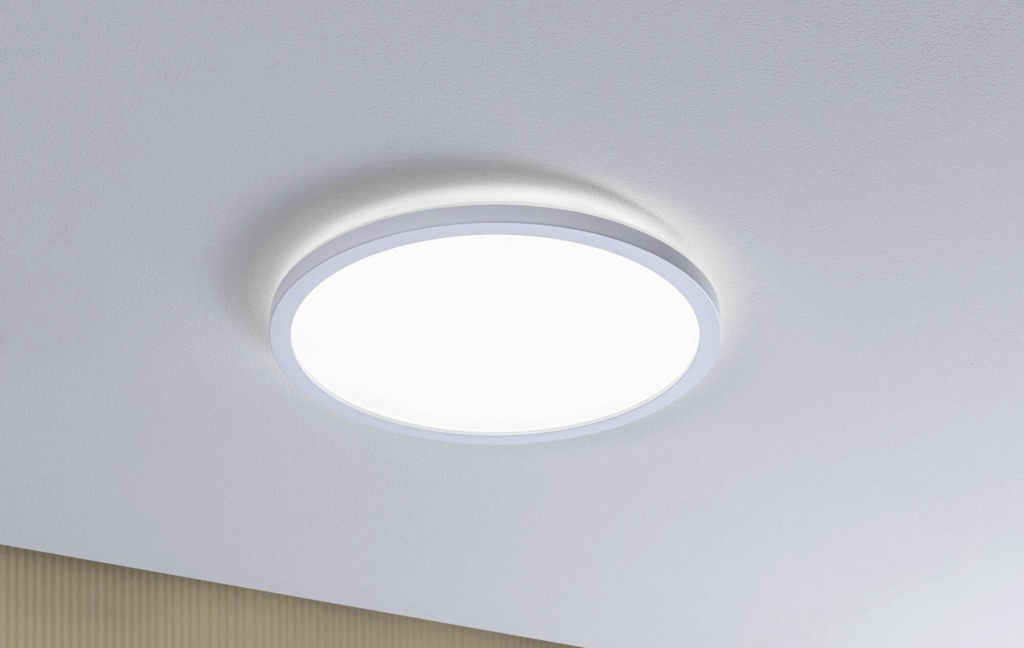 Okrągła, biała lampa sufitowa o delikatnym świetle, zamontowana na jasnym suficie we wnętrzu w nowoczesnym stylu.