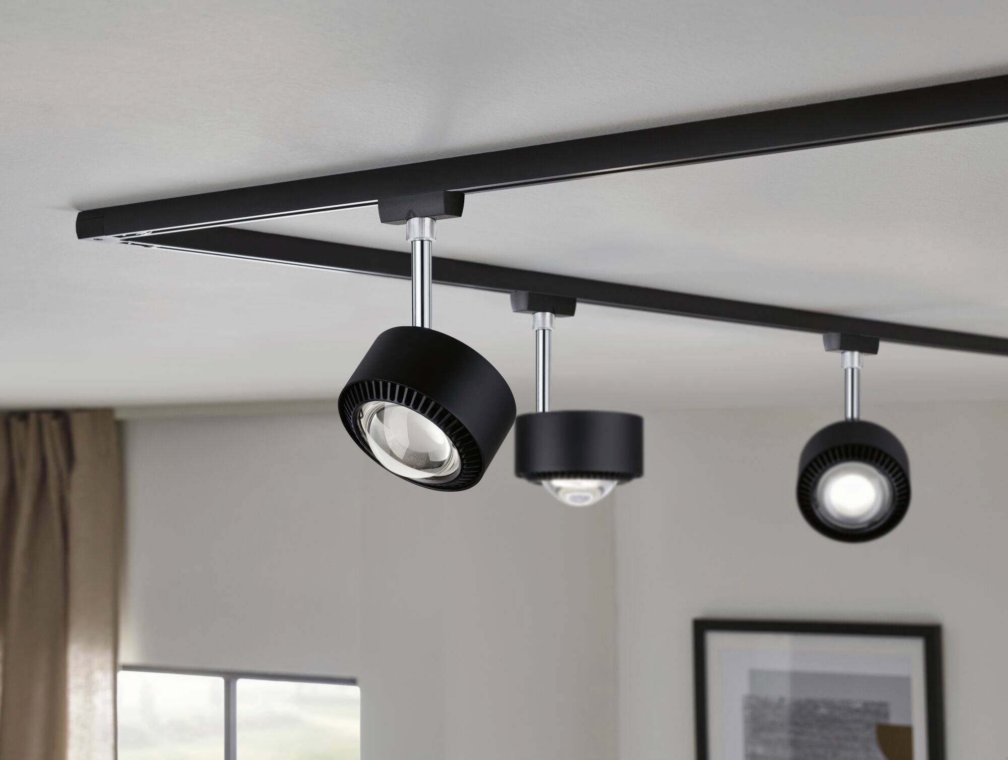Trzy czarne sufitowe reflektory LED są zamontowane na szynie. Oświetlają one przestrzeń we wnętrzu o nowoczesnym designie.