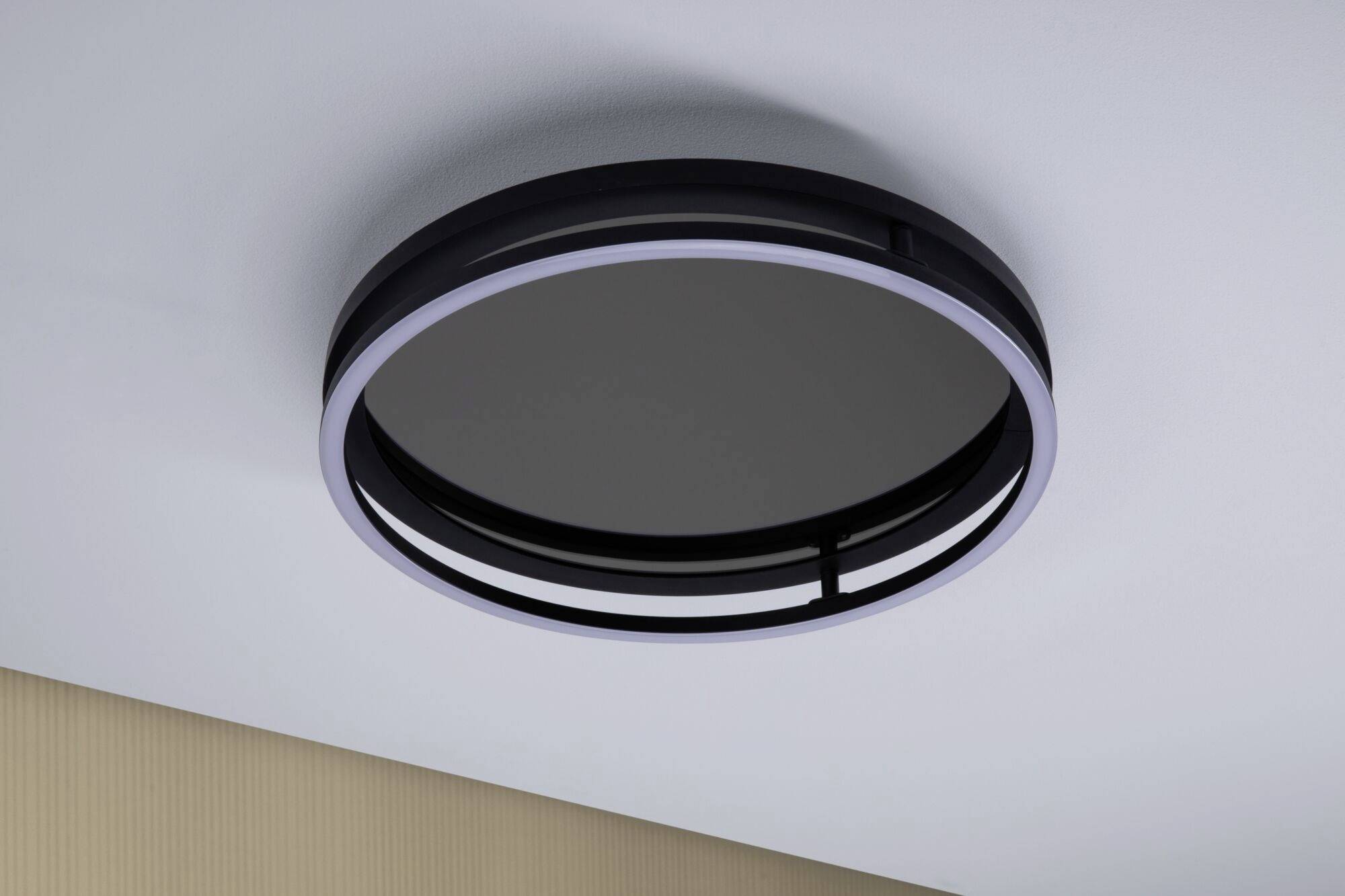 Lampa sufitowa o okrągłym, nowoczesnym designie zamontowana na białym suficie, podświetlona na obrzeżach, idealnie komponująca się z minimalistycznym wystrojem wnętrza.